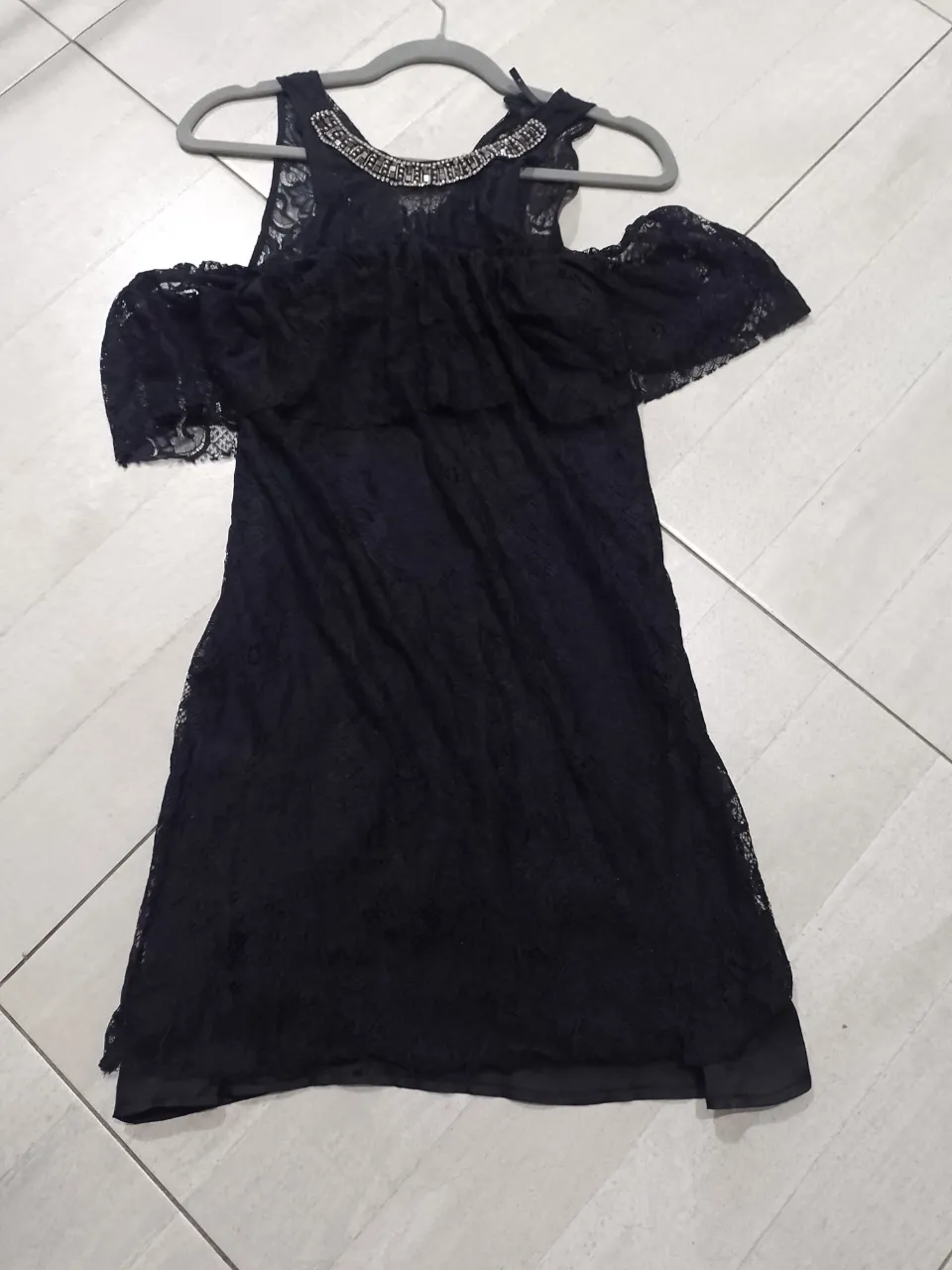 Vestido midi negro de encaje con detalles de pedrería en el cuello y hombros descubiertos y manchitas de encaje superpuestas. Ideal para fiestas y eventos especiales. 