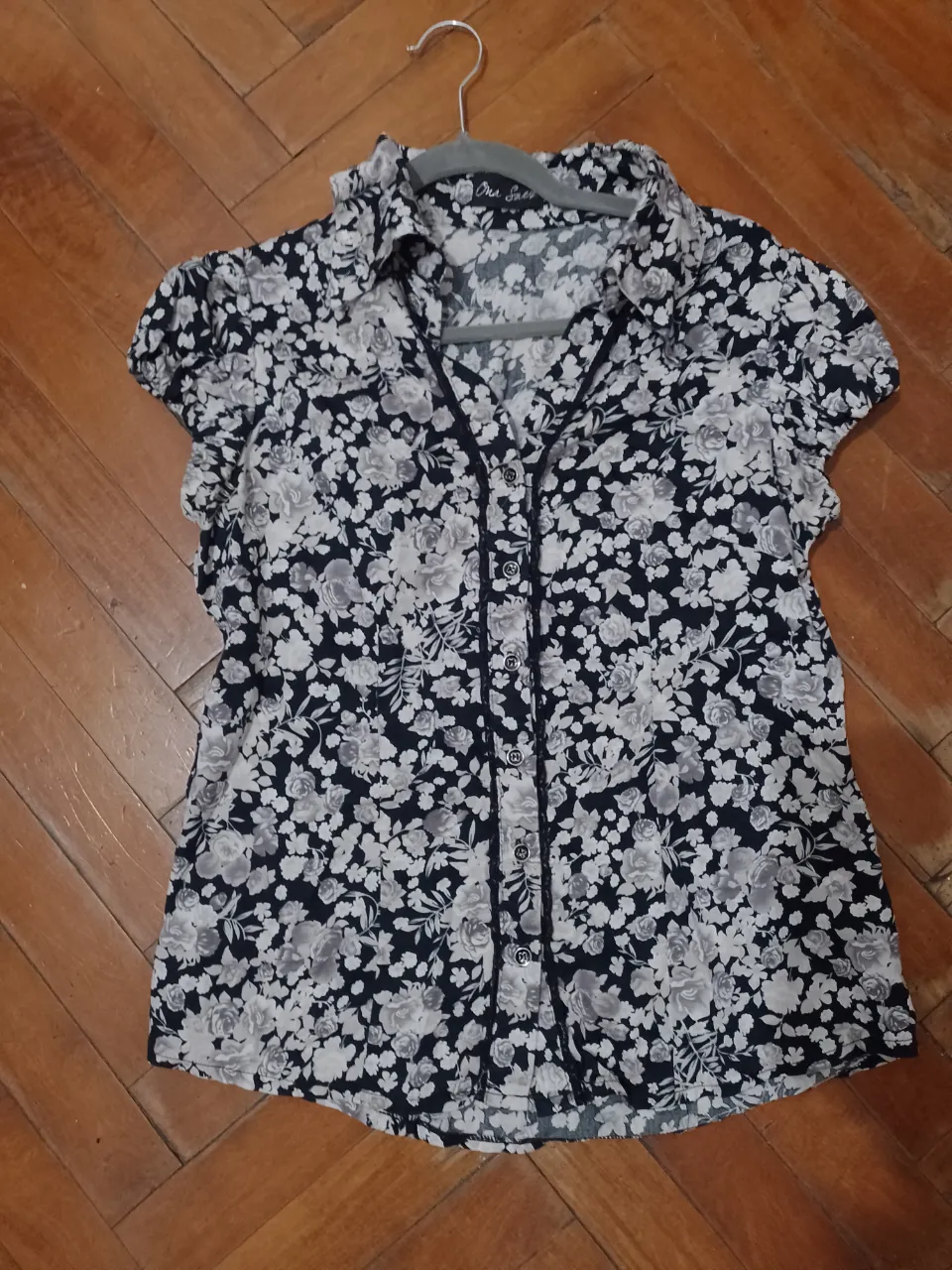 Blusa de mujer con estampado floral en blanco y negro. Confeccionada con tela ligera y fresca, ideal para un look casual y femenino. Cuenta con botones y detalles de encaje