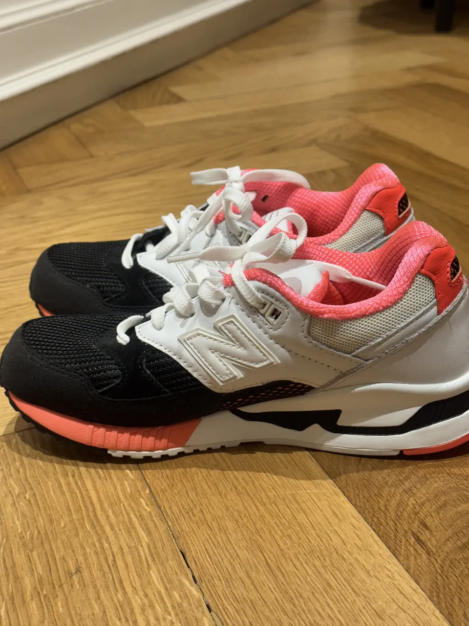 Zapatillas New Balance 530 para mujer, combinan blanco, negro y detalles en rosa. Ideales para un look deportivo y moderno.
