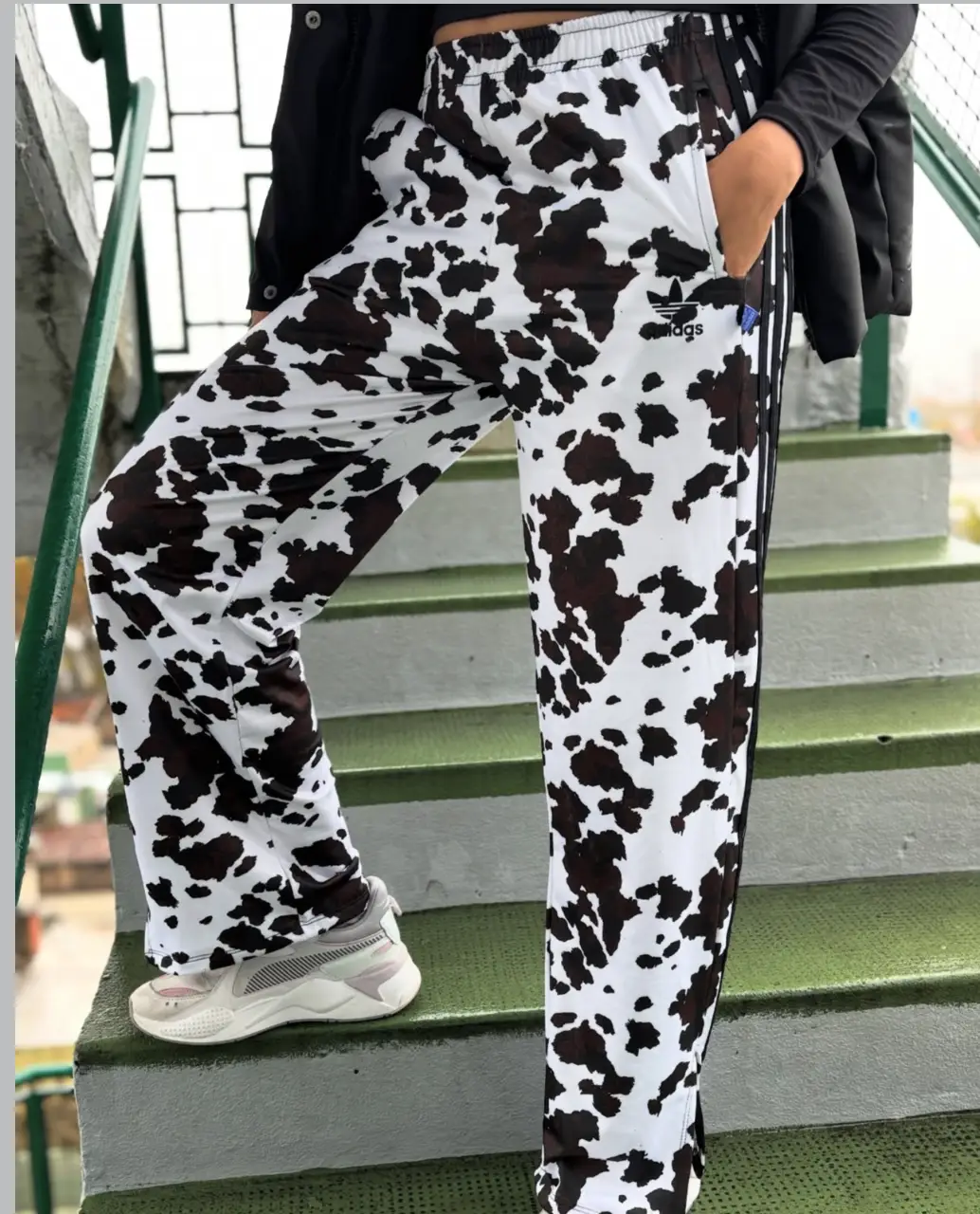 Pantalón deportivo Adidas con estampado de vaca, con las tres tiras en negro a los costados. Ideal para un look canchero y cómodo.