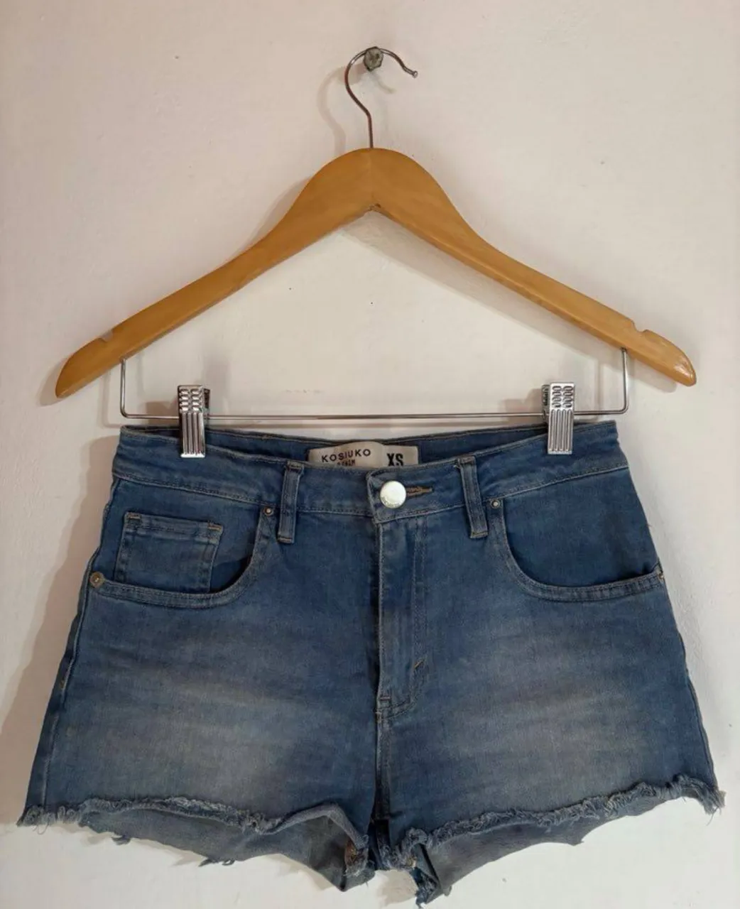 Short de jean azul claro, tiro medio, con detalles de desgaste y flecos en el borde. Ideal para un look casual y moderno.