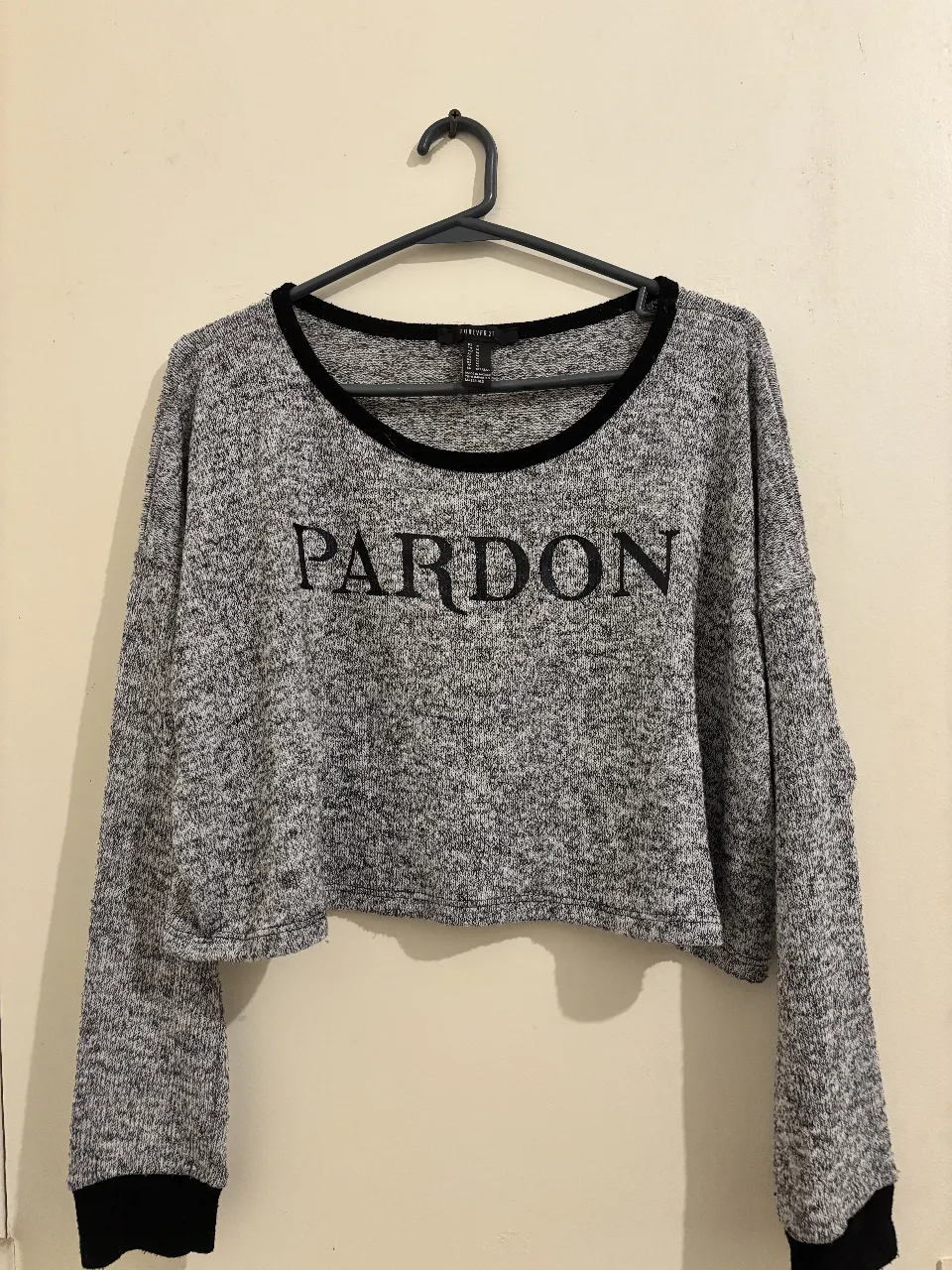 Buzo crop de mujer, color gris con detalles en negro. Con la palabra "PARDON" estampada en el frente. Ideal para un look casual y moderno.