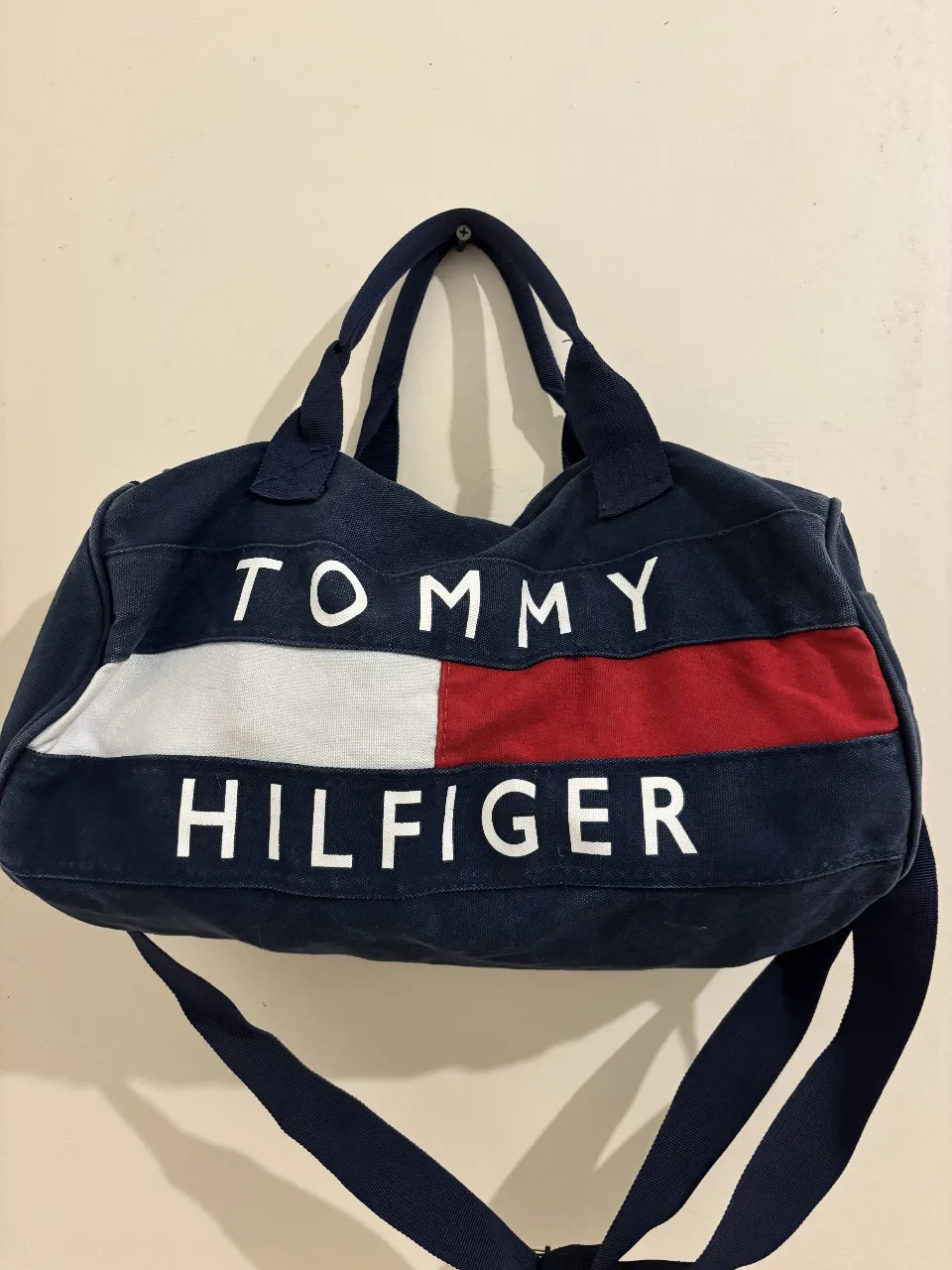Bolso de viaje Tommy Hilfiger azul marino con detalles en blanco y rojo. Ideal para llevar todo lo necesario con estilo y comodidad. Perfecto para viajes cortos o para el gimnasio.