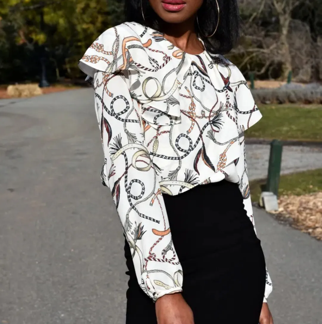 Blusa blanca con estampa de cadenas y cinturones en tonos tierra y negro. Posee volados en los hombros y cuello. Ideal para un look elegante y canchero.