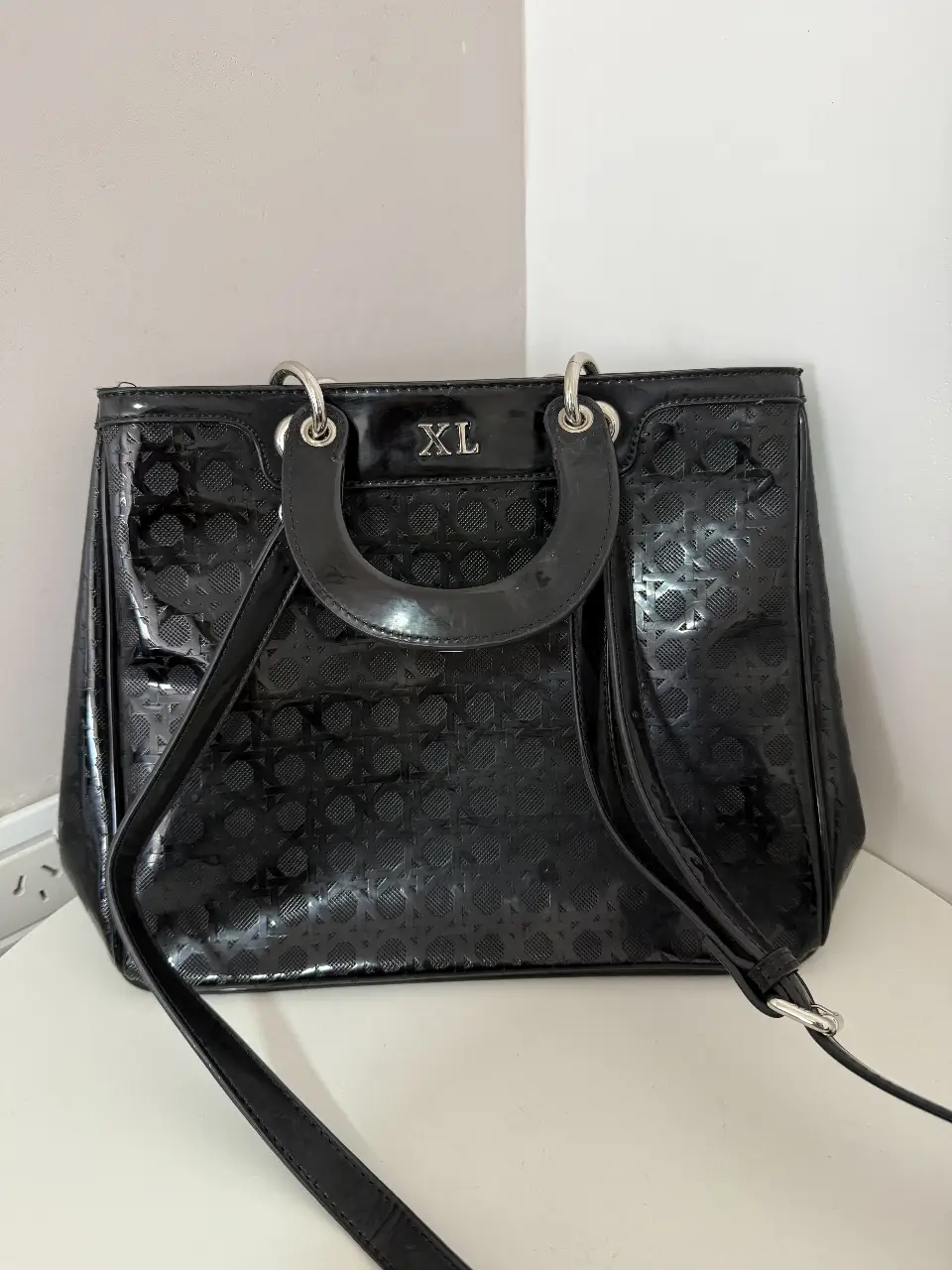 Cartera negra con diseño en relieve y manijas superiores. Ideal para llevar tus esenciales con estilo.