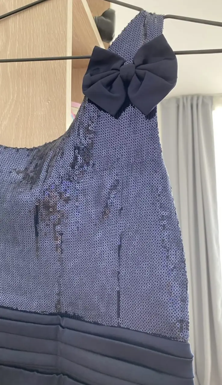 Vestido mini de fiesta, con lentejuelas en la parte superior y un lazo en el hombro. La falda es de un azul oscuro elegante.