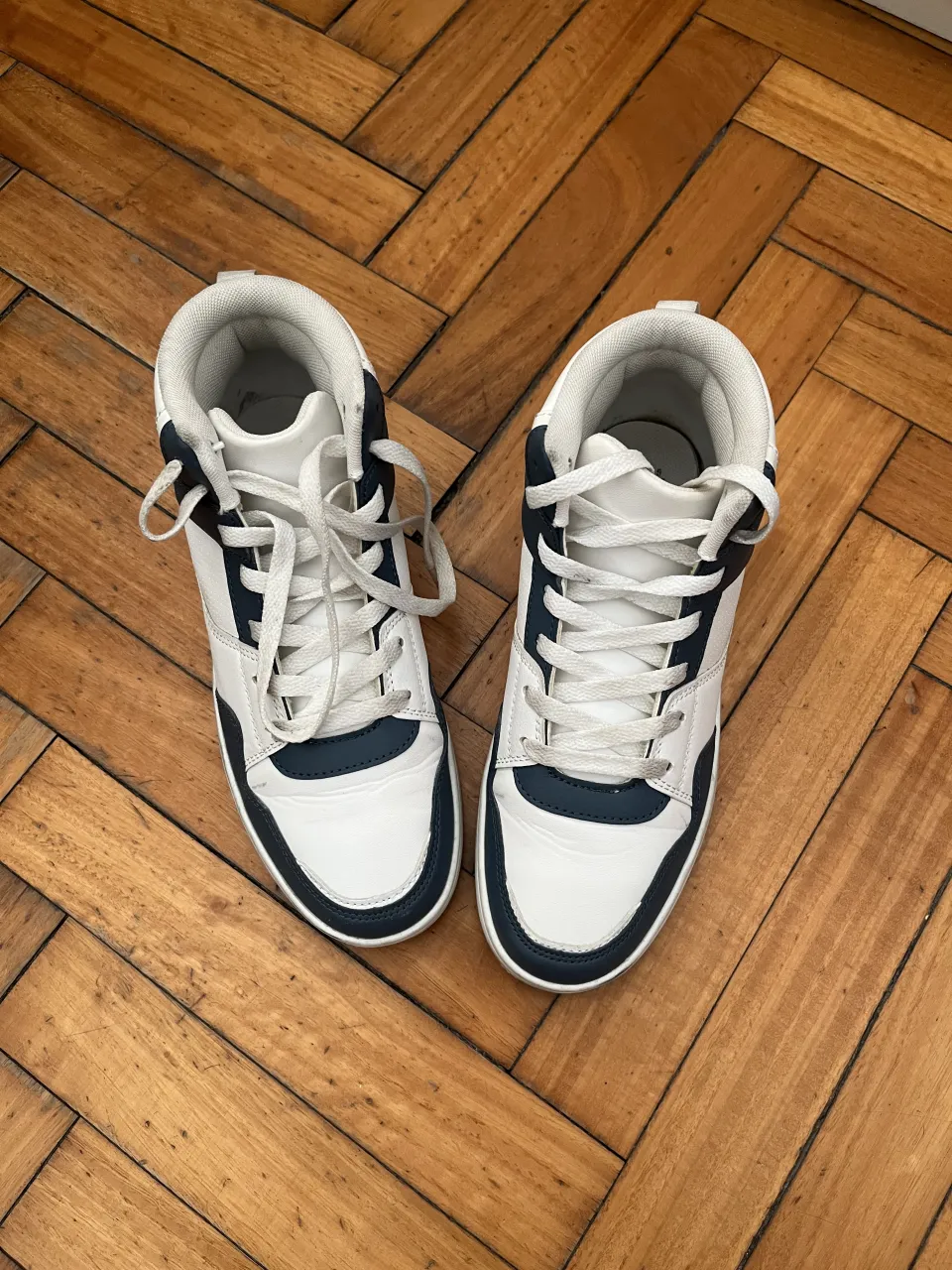 Zapatillas urbanas de caña alta, combinando blanco y azul marino. Cuentan con cordones blancos para un ajuste seguro y una suela blanca.