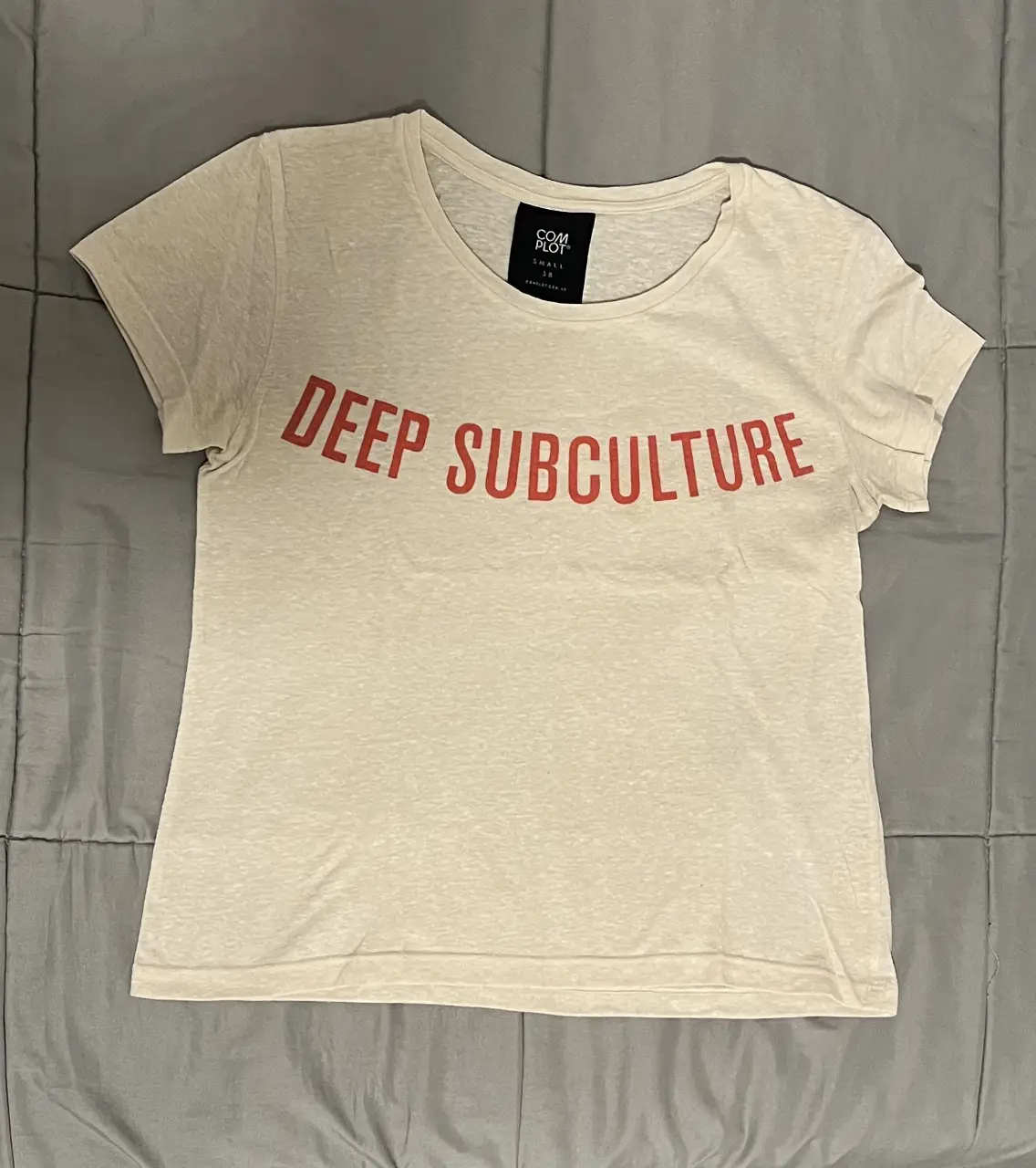Remera de algodón color crudo con estampado "DEEP SUBCULTURE" en rojo. Ideal para un look casual y urbano. Marca: COMPLOT. Talle S.