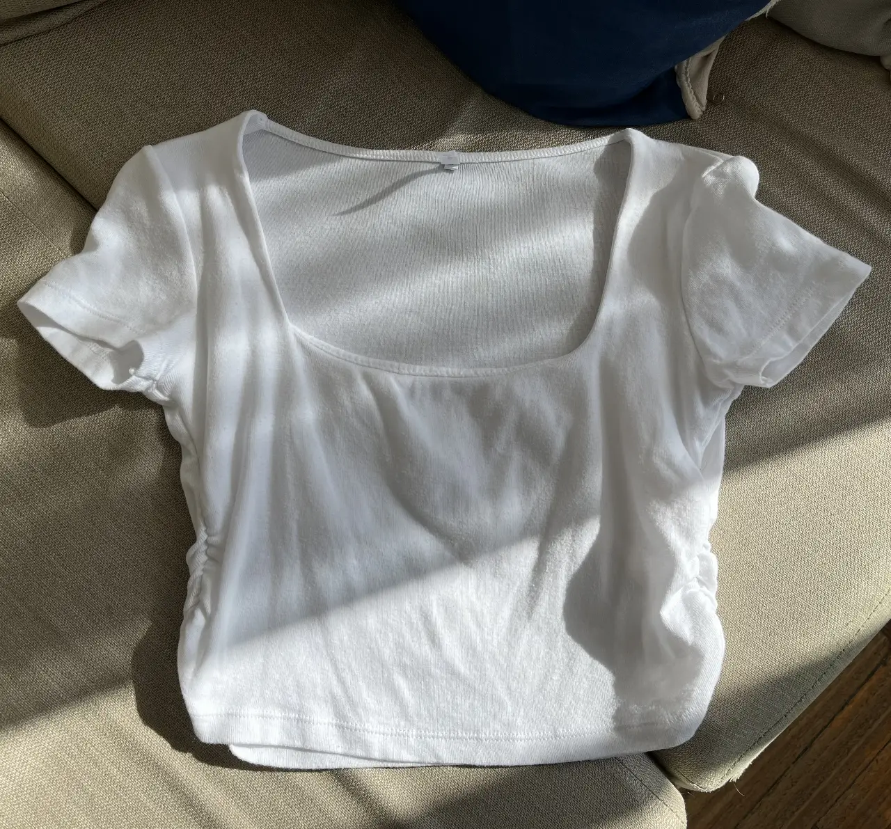 Remera blanca, con cuello cuadrado y detalles fruncidos en los laterales. Ideal para un look casual y moderno.