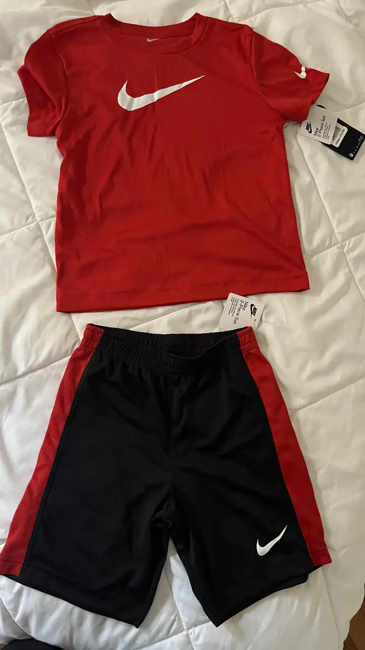 Conjunto deportivo Nike para niño, compuesto por remera roja con logo blanco y short negro con detalles rojos y logo blanco. Ideal para actividades deportivas.