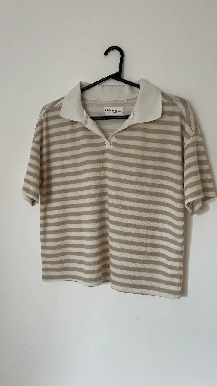 Remera manga corta a rayas horizontales en tonos crudo y marrón. Cuello polo con solapa en color crudo. Ideal para un look casual y fresco. Medidas: ancho 53 cm largo 52 cm 