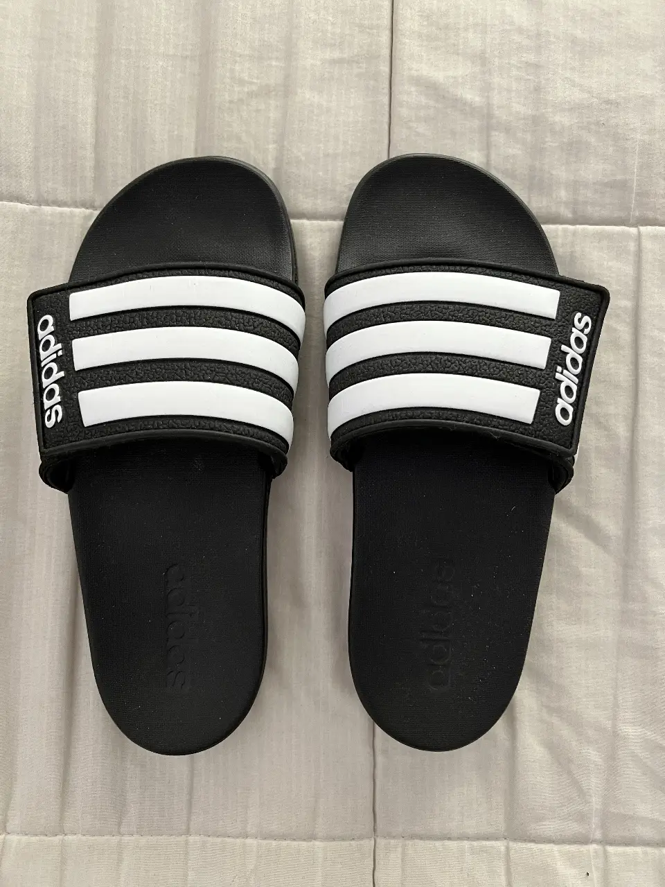 Ojotas Adidas Adilette con las tres tiras blancas características de la marca. Ideales para la playa, pileta o uso diario. Cómodas y con el logo de Adidas en la tira.