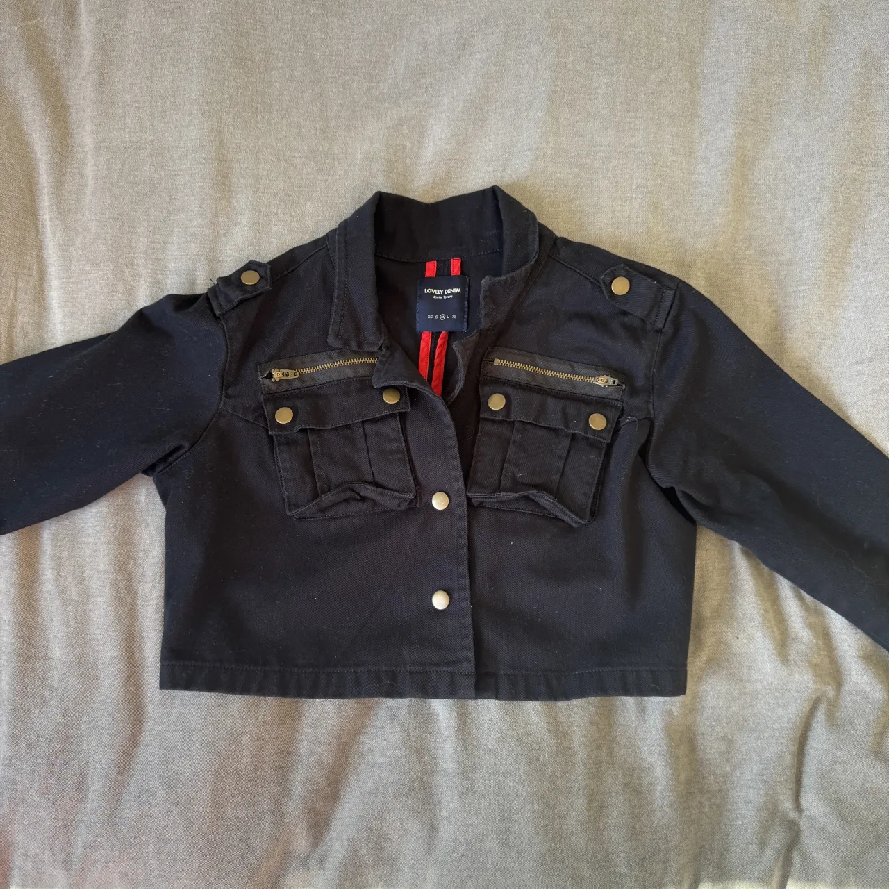 Campera negra corta estilo militar, con detalles de bolsillos y cierres dorados. 