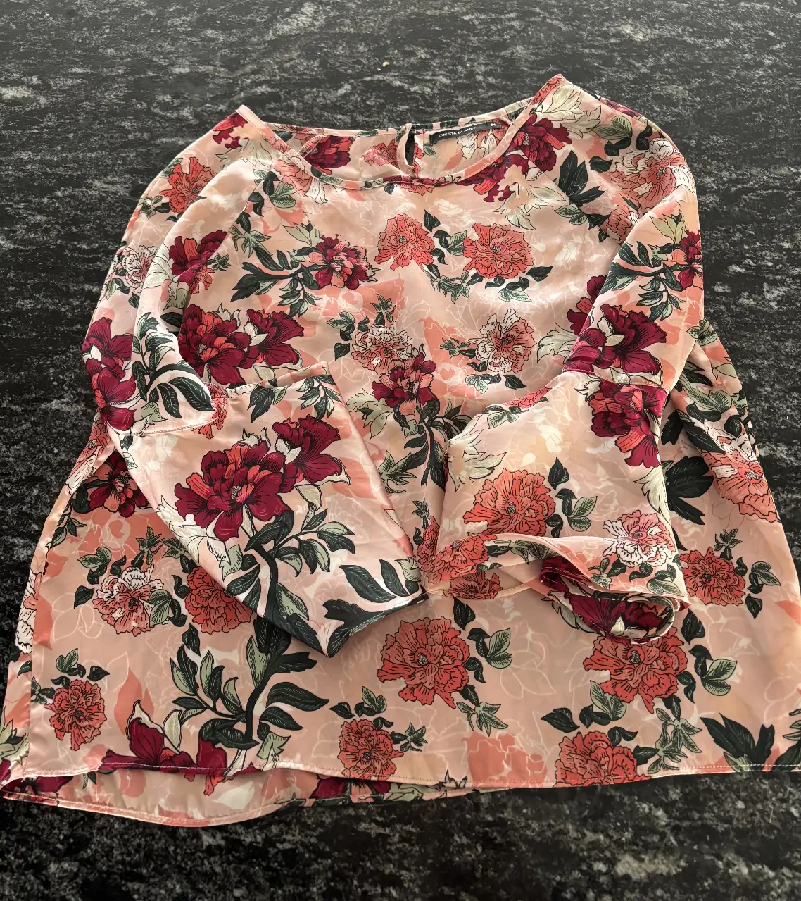Blusa de mujer con estampado floral en tonos rosados y rojos. Tiene mangas largas con volados y un cuello redondo. Ideal para un look elegante y femenino.