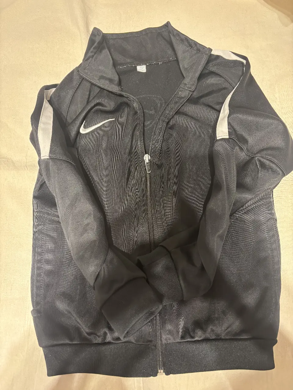 Campera deportiva Nike negra con detalles blancos. Ideal para entrenar o usar en el día a día. Con cierre y logo de la marca.
