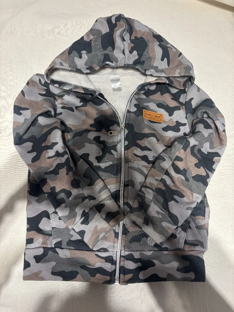 Buzo con cierre para niño, con estampado de camuflaje en tonos grises y marrones. Posee capucha y bolsillos delanteros. Ideal para un look casual y abrigado.