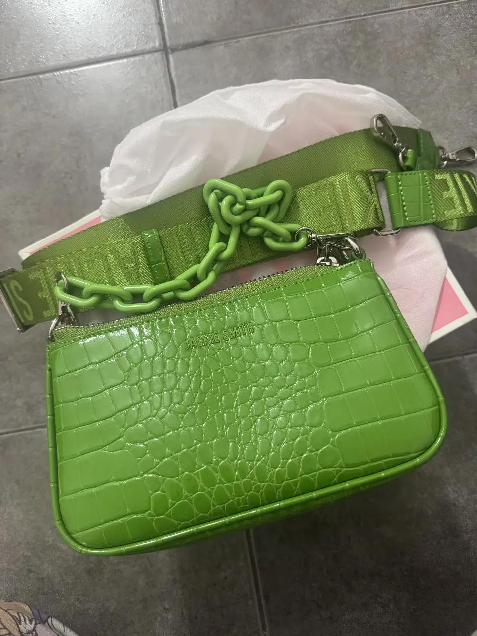 Cartera Jackie Smith verde, con textura de cocodrilo. Incluye correa larga y cadena para llevar al hombro o cruzada. Interior con forro a rayas blanco y negro.