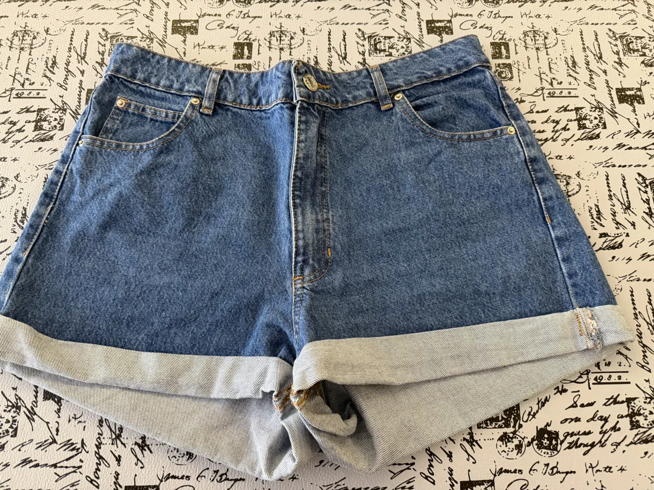 Shorts de jean tiro alto, color azul. Poseen dobladillo en los bordes inferiores.