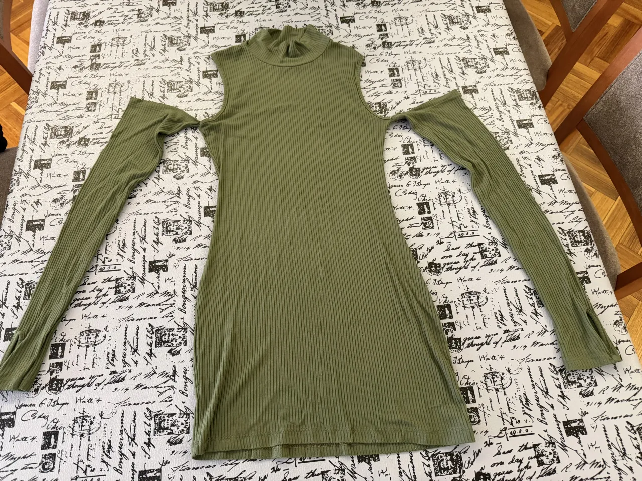 Vestido verde con cuello alto y mangas largas. Posee recortes en los hombros y aberturas en los puños.