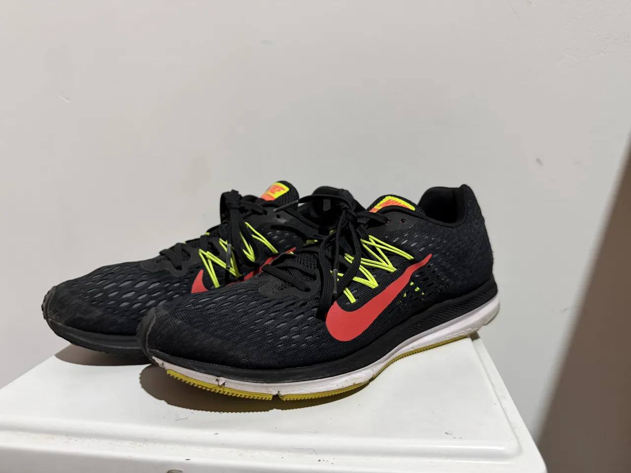 Zapatillas deportivas Nike negras con detalles en rojo y amarillo. Cordones negros y suela blanca con detalles amarillos.