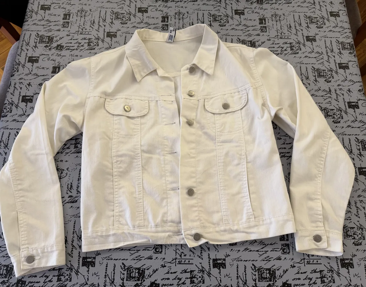 Campera de jean blanca, con botones metálicos al frente y en los puños. Posee dos bolsillos superiores con tapa y botones, y dos bolsillos inferiores sin tapa.