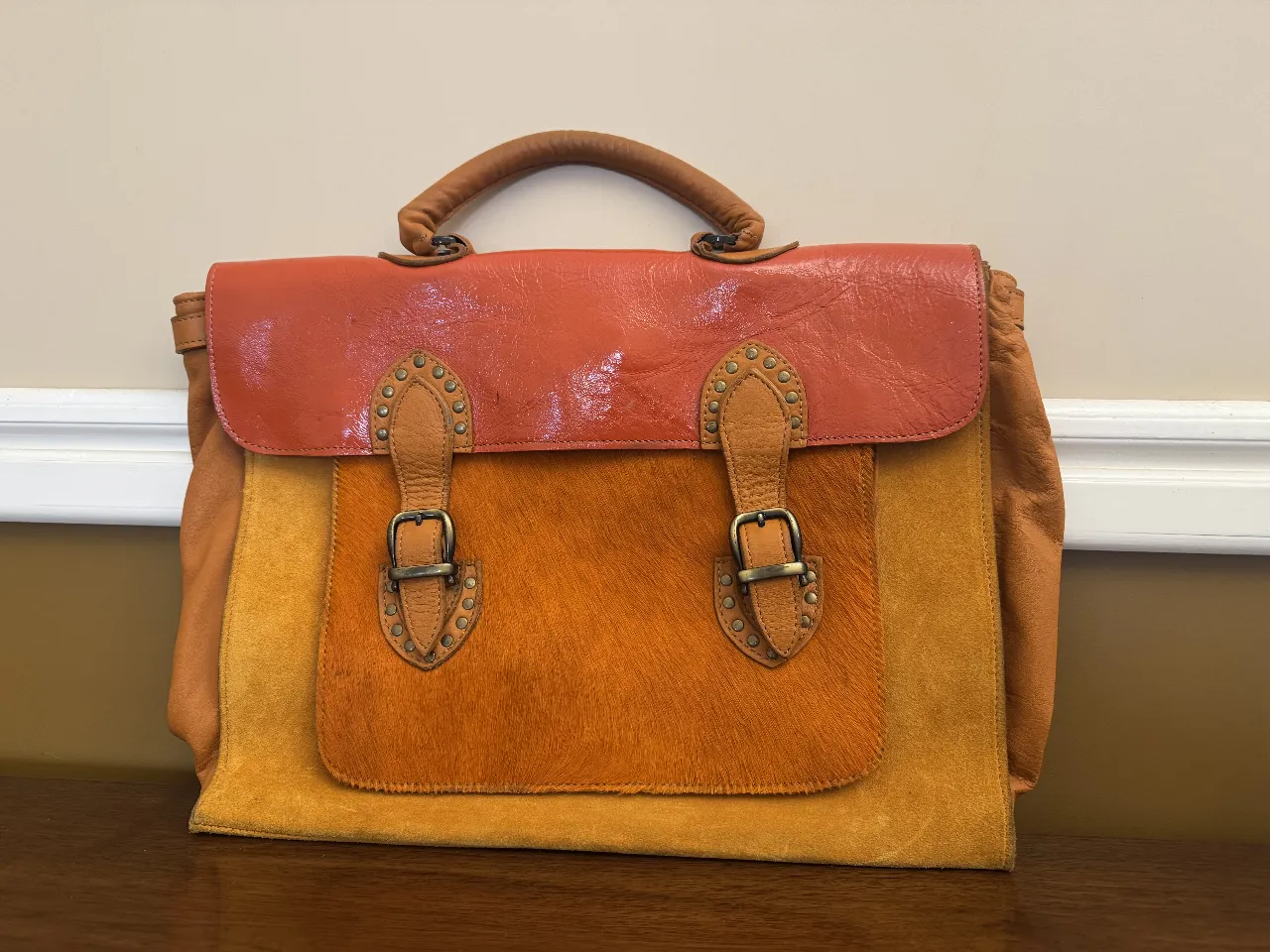 Cartera de cuero con solapa en color naranja y cuerpo en gamuza amarilla. Detalles de hebillas y tachas. Ideal para un look vintage y con estilo.