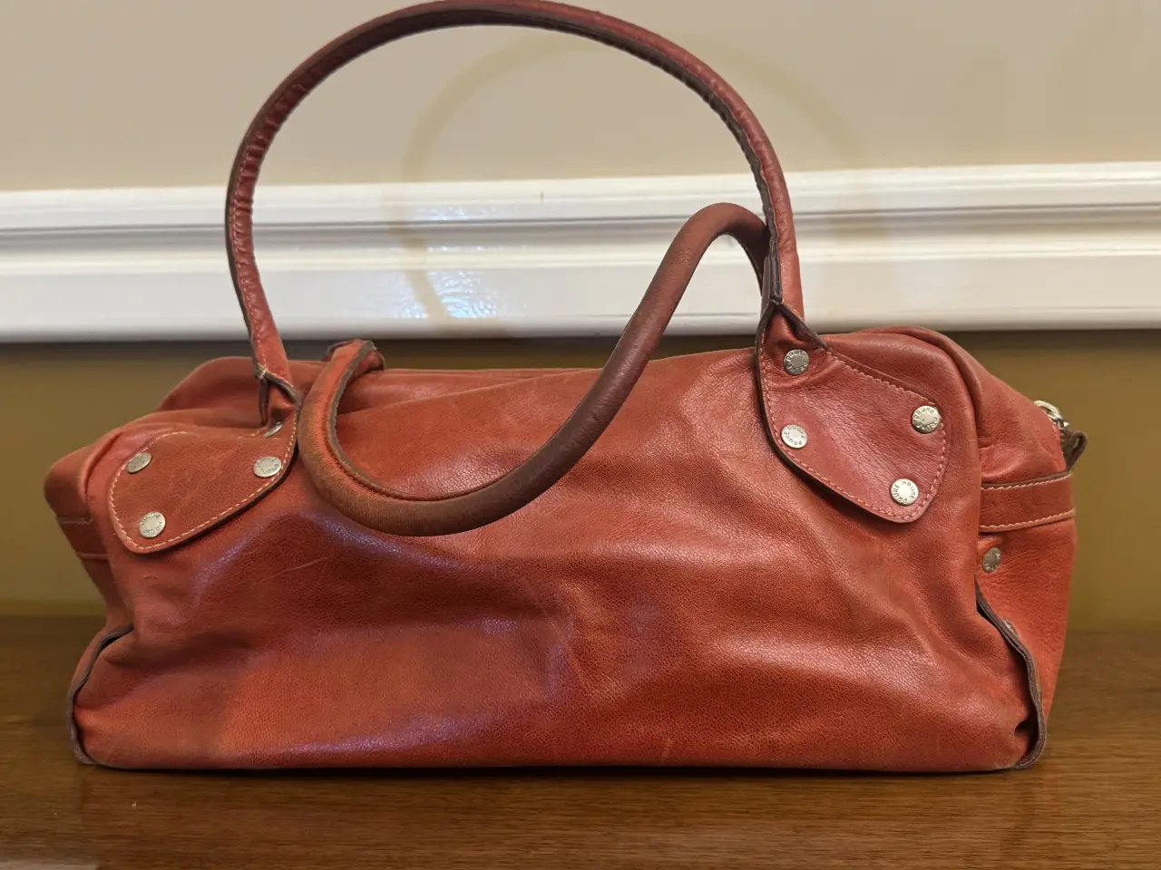 Cartera de cuero naranja con manijas y detalles plateados. Ideal para llevar tus esenciales con estilo y un toque vintage.