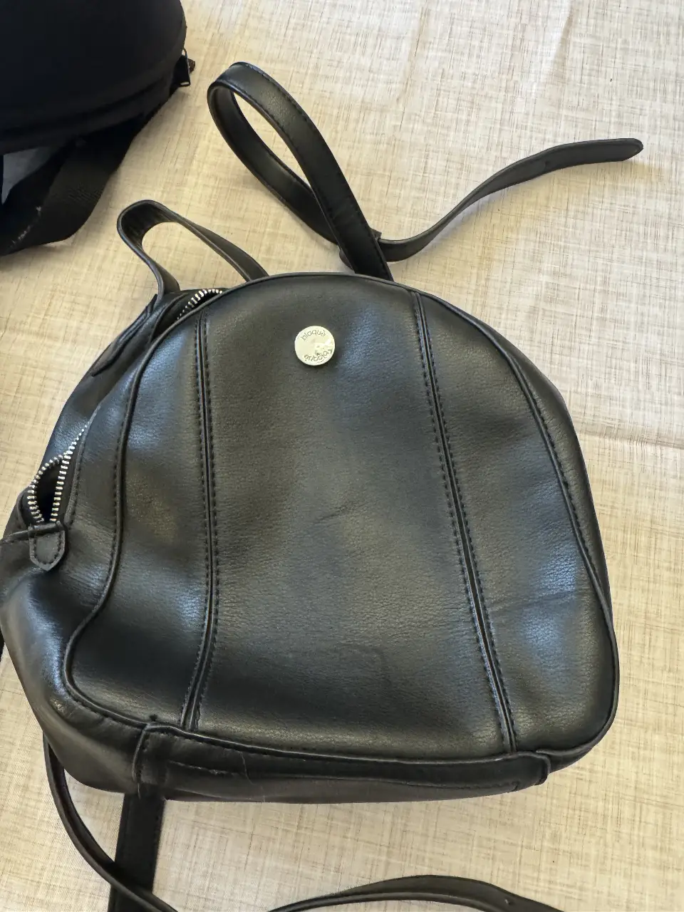 Mochila negra de cuero sintético, ideal para uso diario. Diseño clásico y versátil, con cierre y detalles de costura. Perfecta para llevar tus esenciales con estilo.