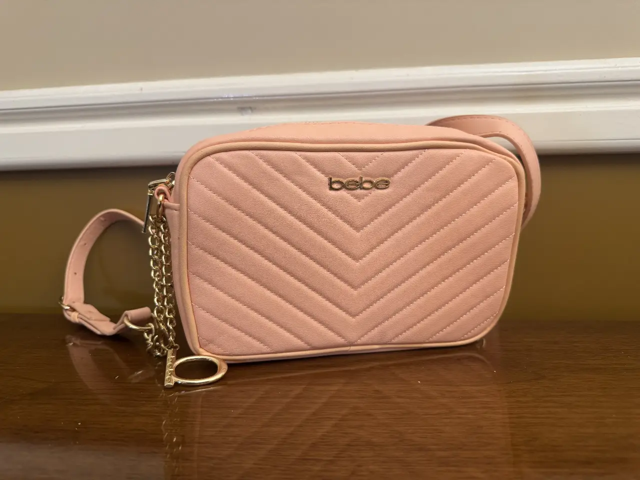 Cartera bandolera rosa bebe acolchada con cadena dorada y logo de la marca. Ideal para un look casual y femenino.