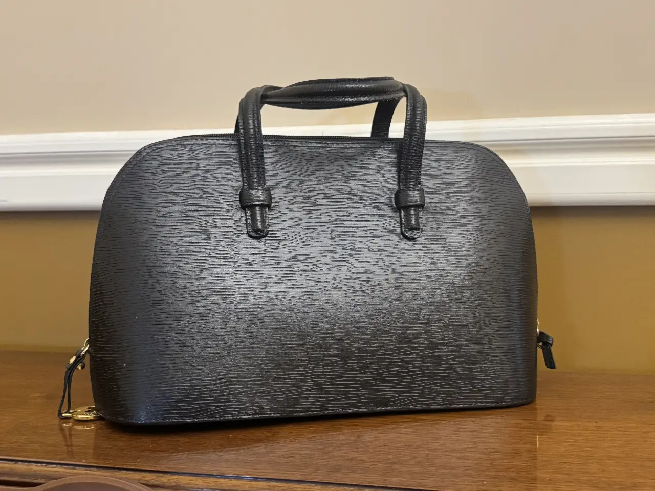 Cartera negra estructurada con manijas cortas y detalles dorados. Ideal para llevar tus esenciales con estilo y elegancia. Perfecta para cualquier ocasión.