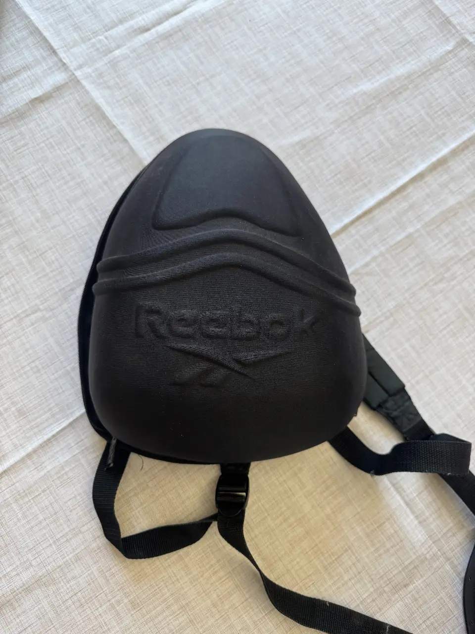 Mochila deportiva negra Reebok, ideal para transportar elementos de protección. Cuenta con correas ajustables y un diseño ergonómico.