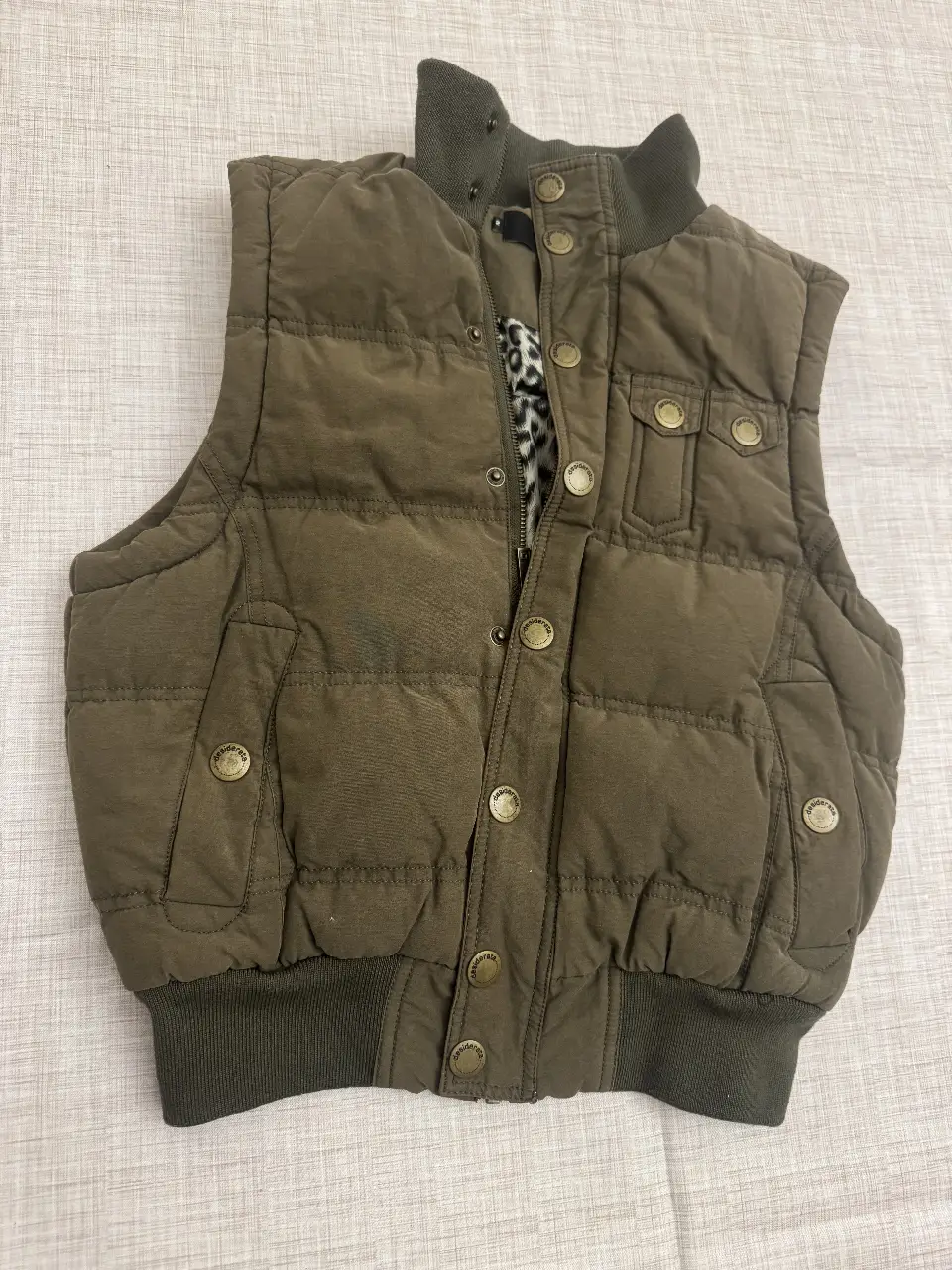 Chaleco acolchado para hombre, color verde oscuro. Diseño con cuello alto y cierre con botones. Interior con forro de estampado animal print. Ideal para un look casual y abrigado.