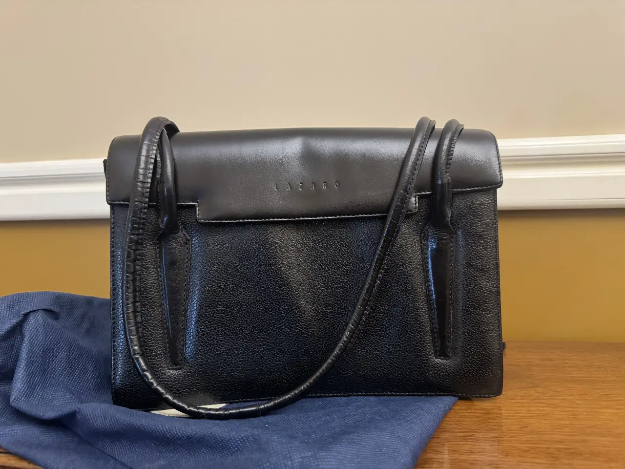 Cartera Lazaro negra de cuero, con manijas y correa para colgar. Ideal para llevar tus esenciales con estilo y elegancia.