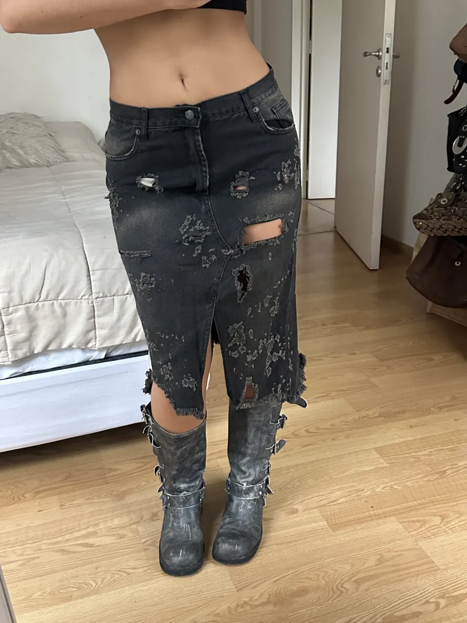 Pollera de jean larga, color negro desgastado, con roturas y detalles deshilachados en toda la prenda. Posee tajos laterales y detalles de tela rasgada.