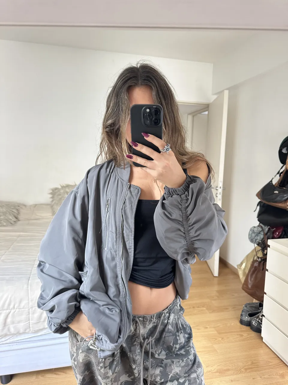 Campera bomber gris con puños y cintura elastizados. Posee bolsillos laterales con botones a presión y un bolsillo con cierre en el frente. Mangas con frunces. Tipo oversize