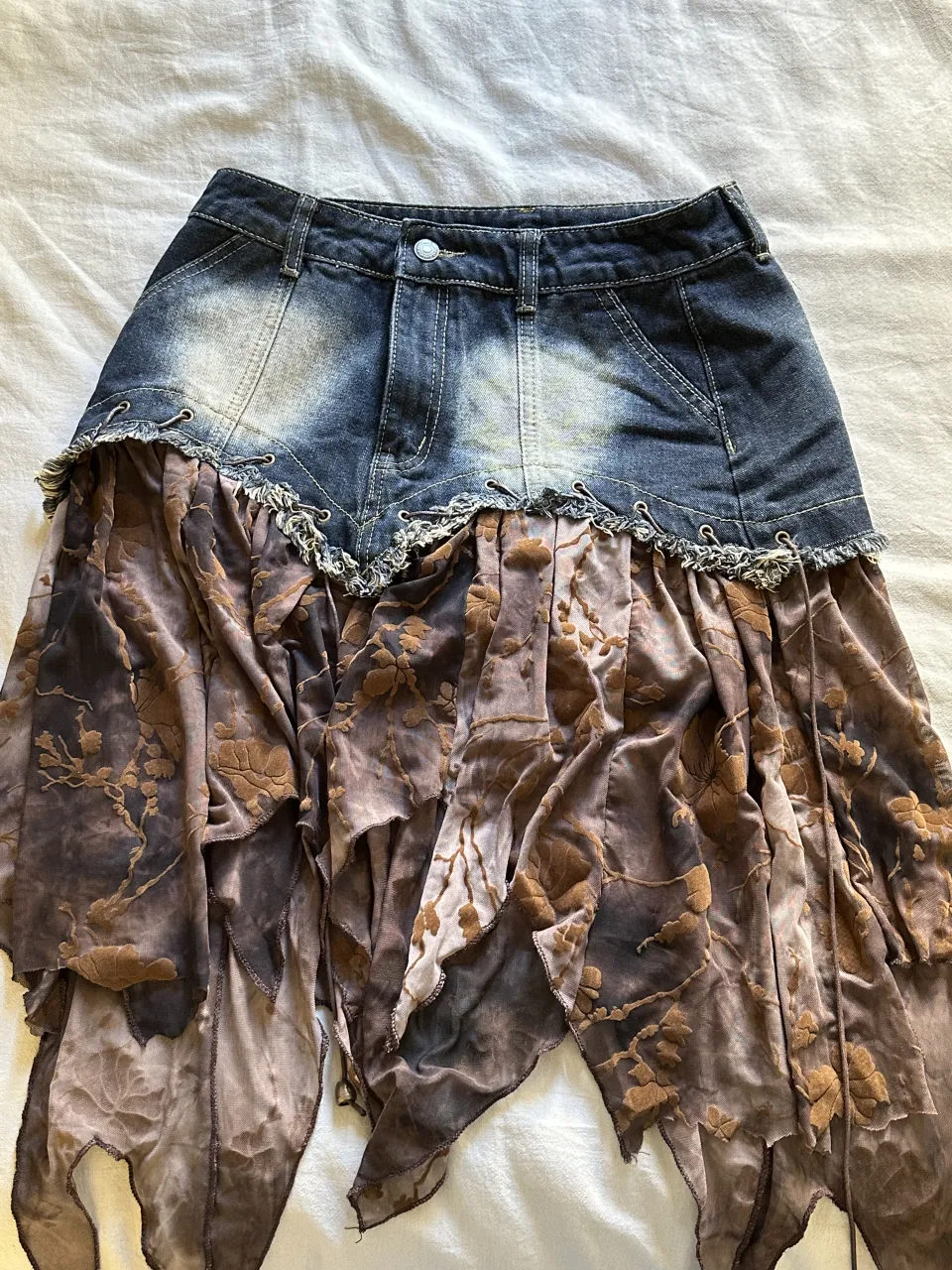 Pollera de jean con detalles de tela estampada y deshilachada en la parte inferior. La parte superior es de jean con lavado desgastado y detalles de costuras.