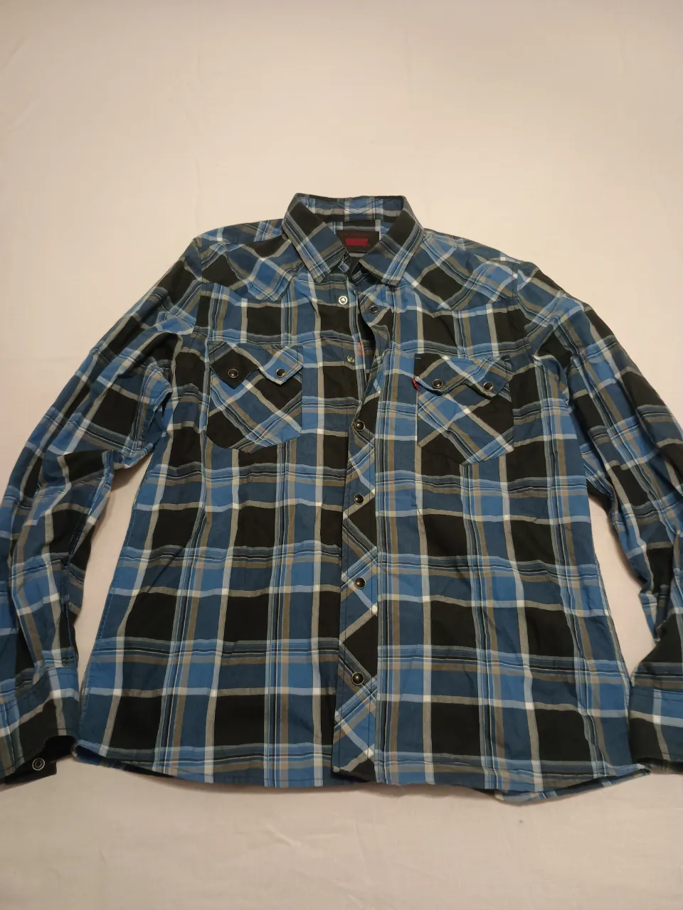 Camisa a cuadros de manga larga con botones al frente. Presenta dos bolsillos en el pecho con solapa y botón. Cuello clásico.