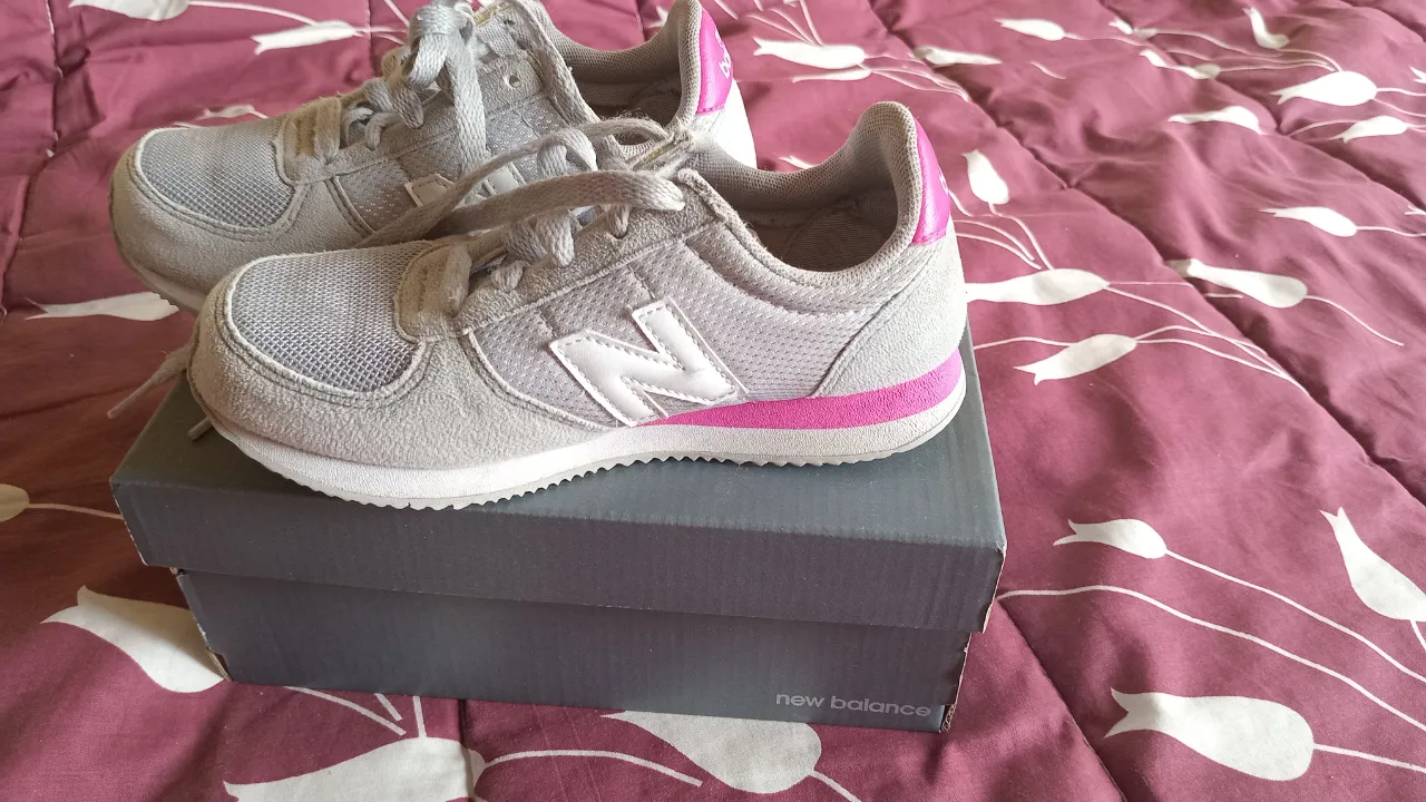 Zapatillas New Balance para niña, color gris con detalles en rosa y blanco. Ideales para uso diario y actividades deportivas.