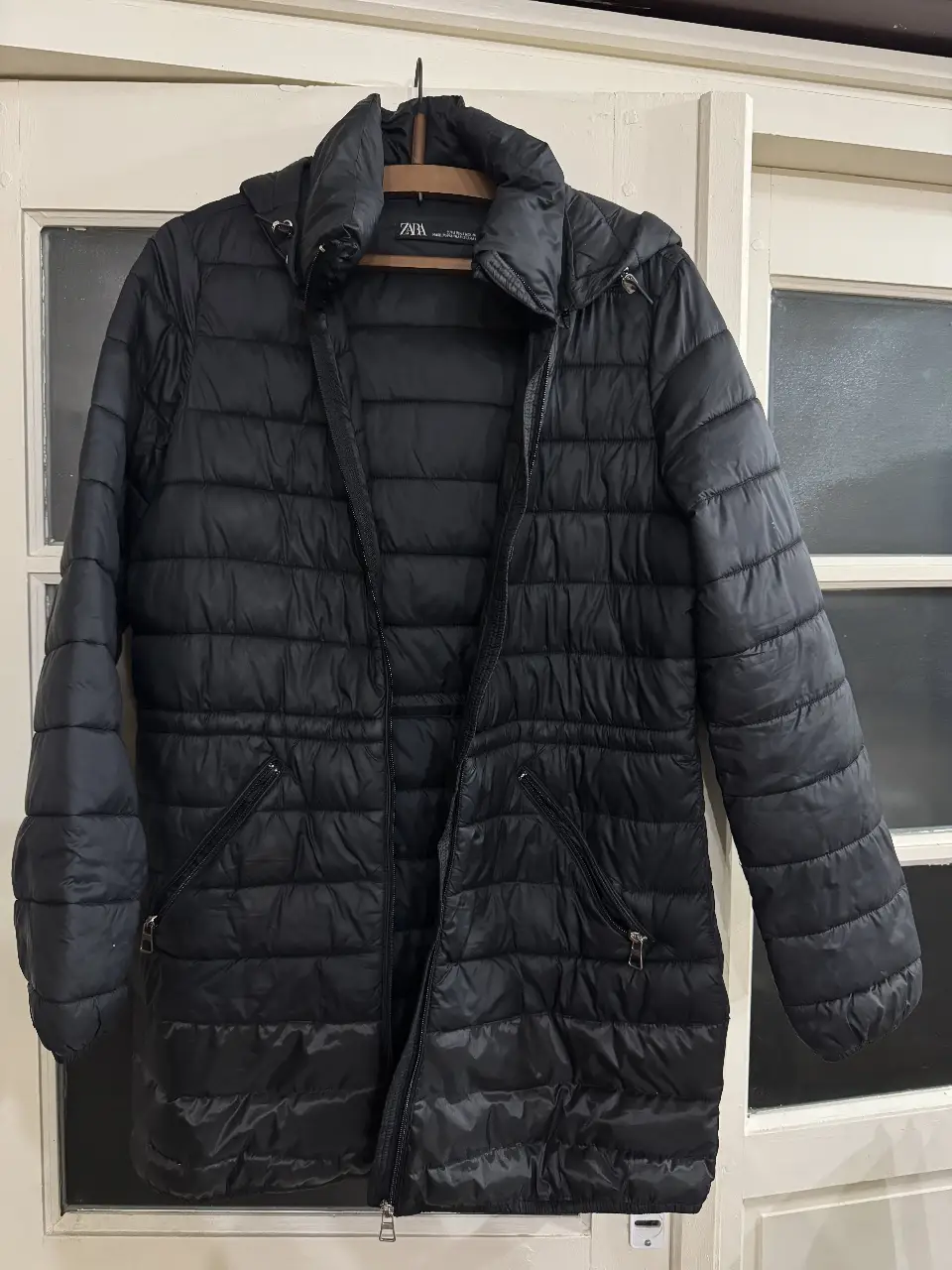 Campera de pluma negra de la marca Zara, con capucha y cierre frontal. Ideal para el invierno, con bolsillos con cierre y un diseño acolchado.