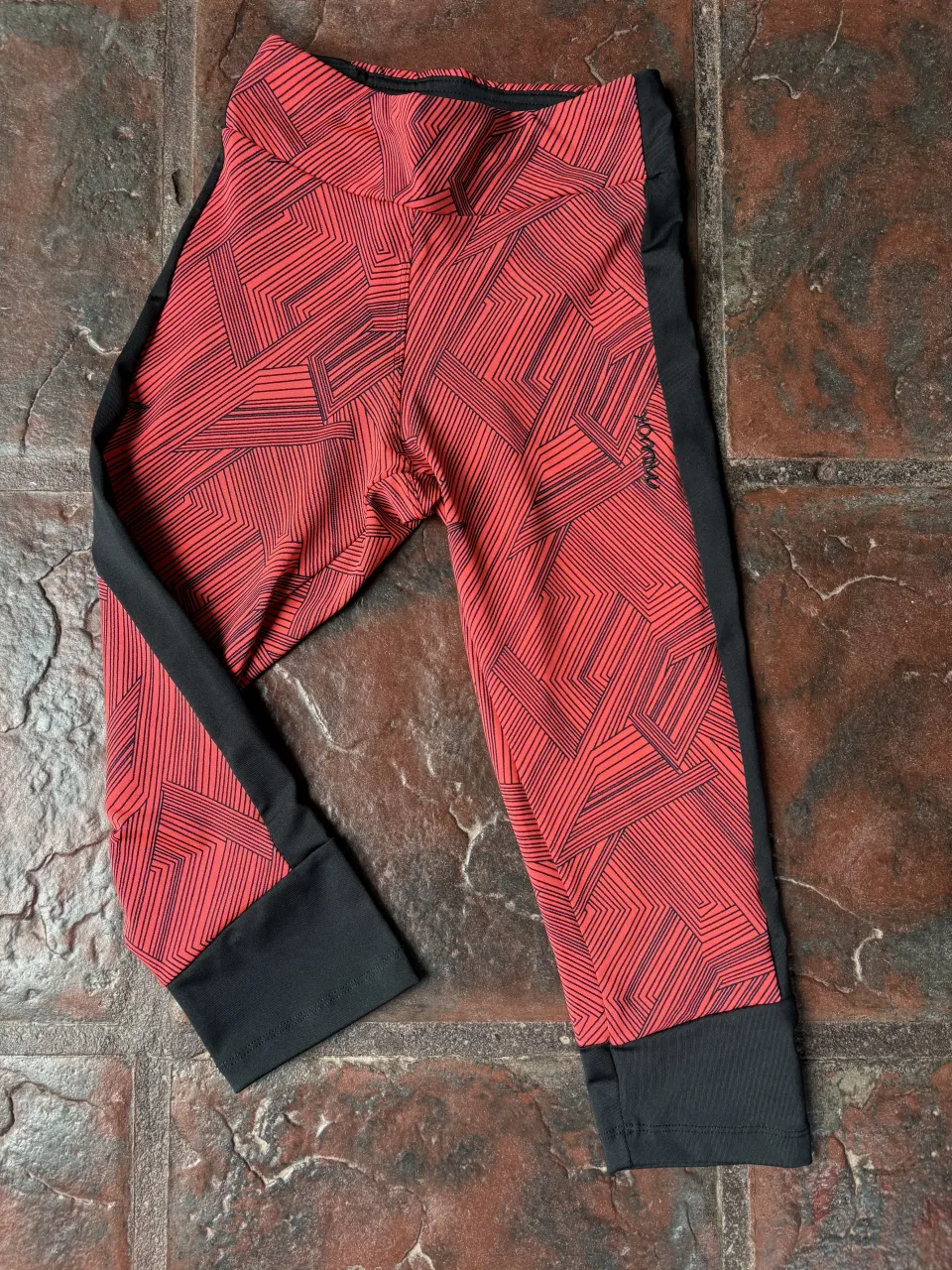 Calzas deportivas cortas con un estampado geométrico en rojo y negro. Ideales para entrenar o para un look casual y cómodo.