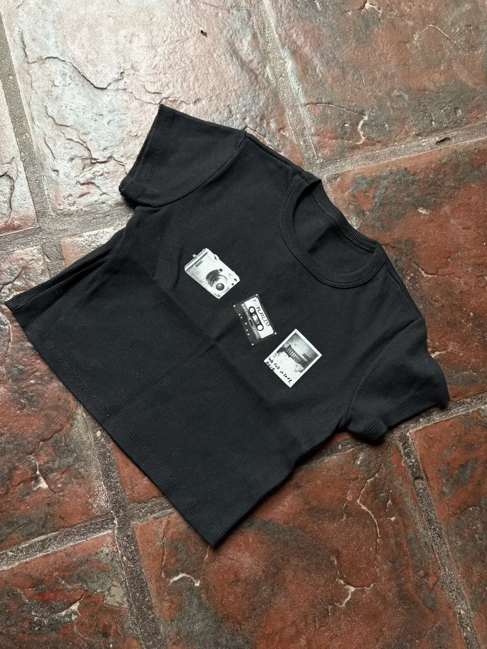 Remera negra con estampa de cámara fotográfica, cassette y foto vintage. Ideal para un look casual y retro.