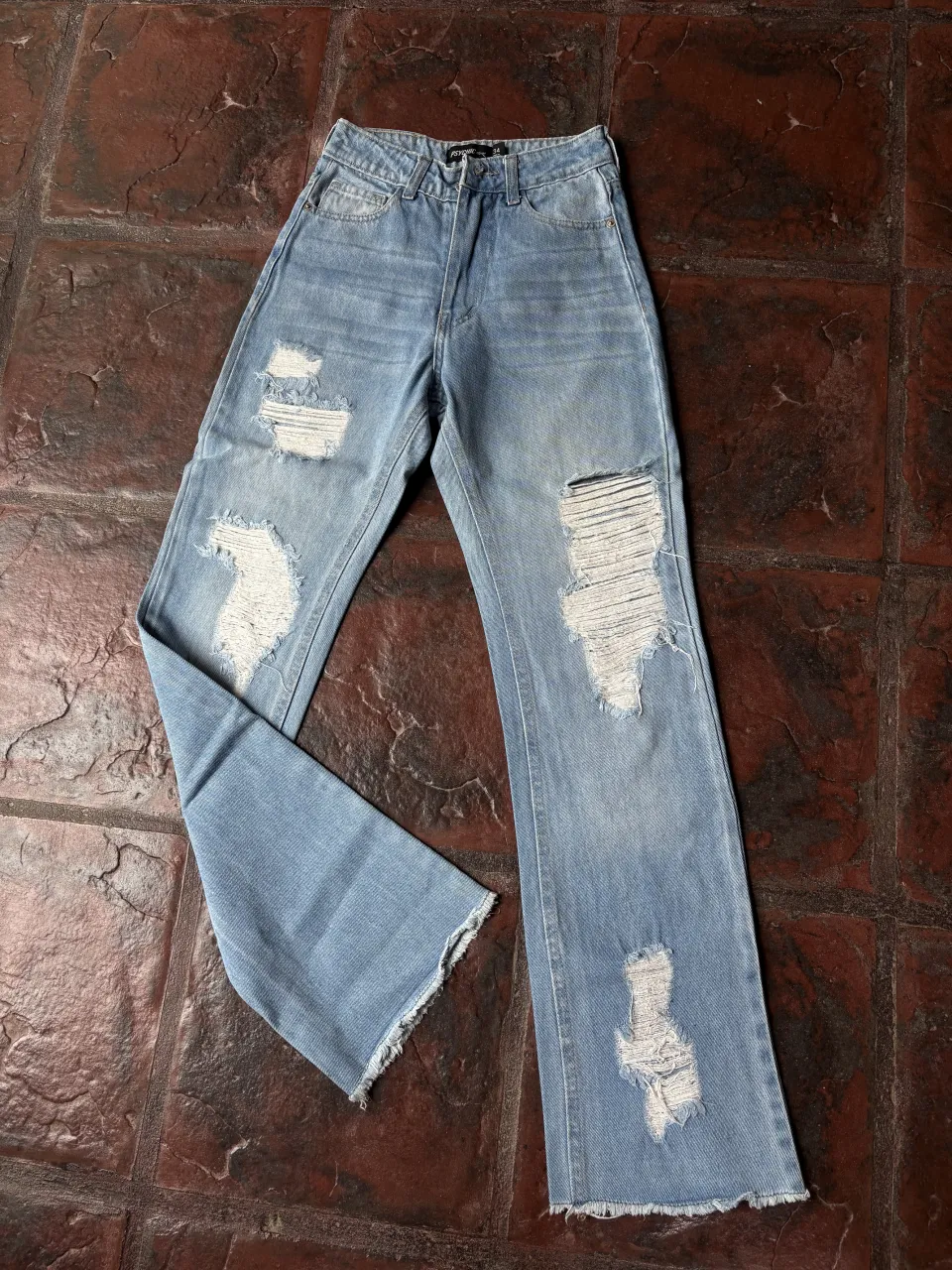 Jean de tiro alto, corte recto y ancho, con roturas desgastadas y detalles desflecados en los bajos. Un estilo moderno y canchero, perfecto para un look relajado.