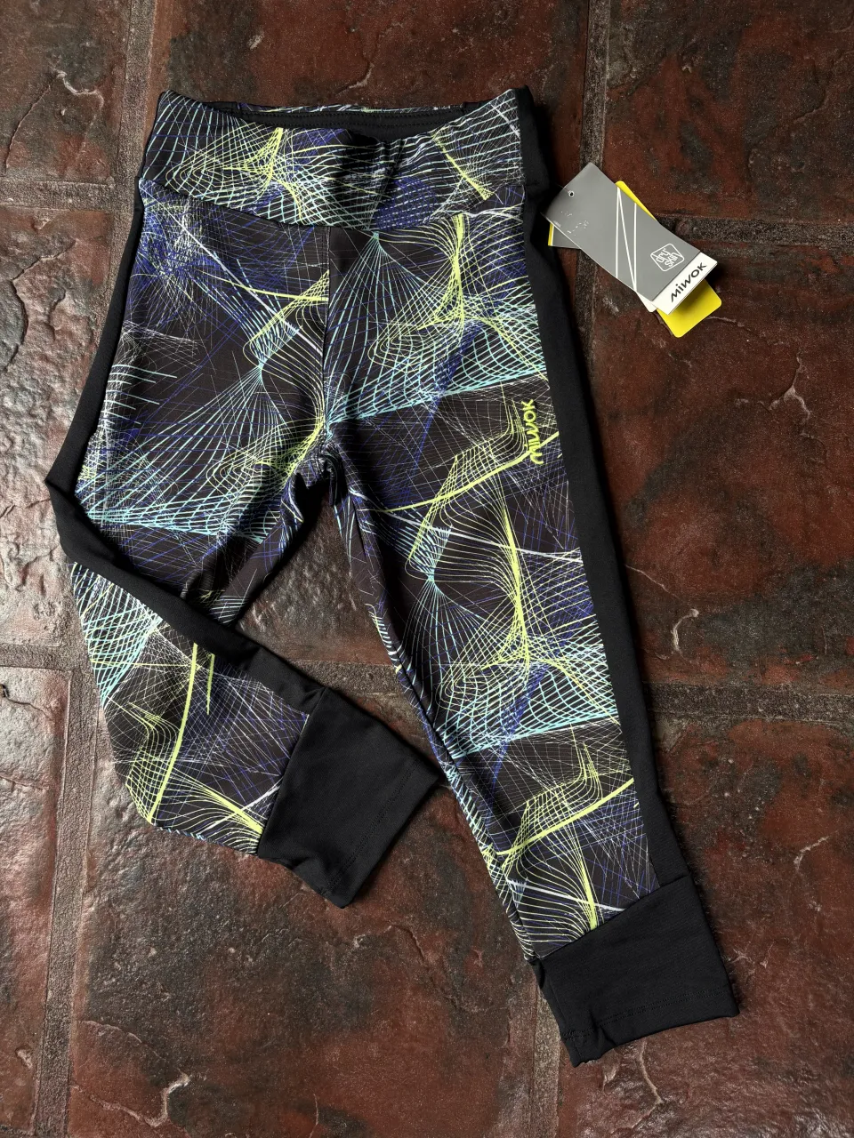 Calzas deportivas con un estampado abstracto en tonos azules y verdes sobre fondo negro. Ideales para entrenar o para un look casual y moderno.