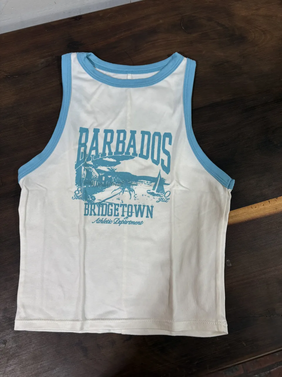 Musculosa blanca con estampa "Barbados Bridgetown Athletic Department" en color azul. Tiene detalles en azul en el cuello y los breteles. Ideal para un look casual de verano.