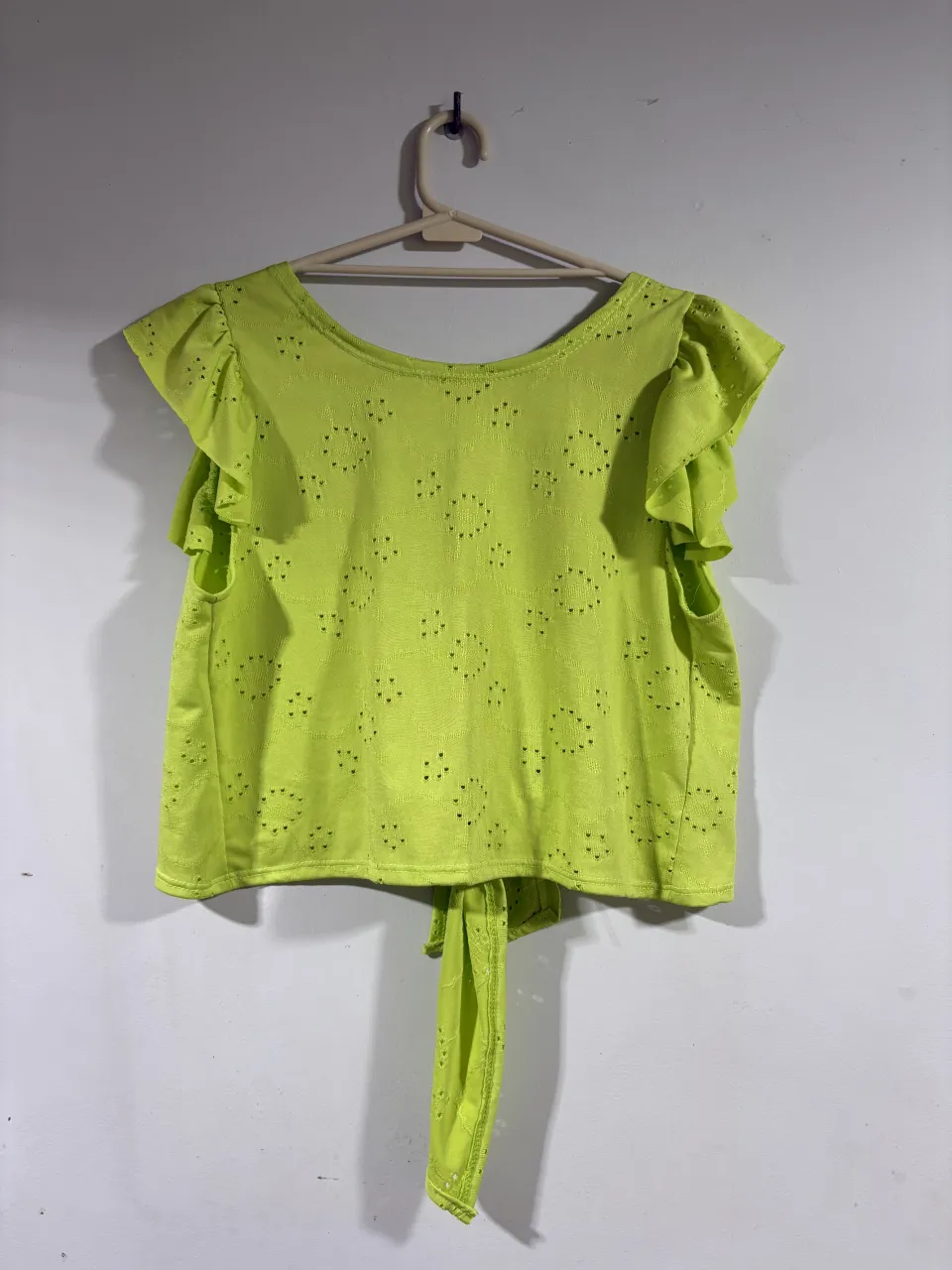 Remera verde lima con mangas cortas con volados y detalle de puntillas. Tiene un lazo en la parte trasera para atar.