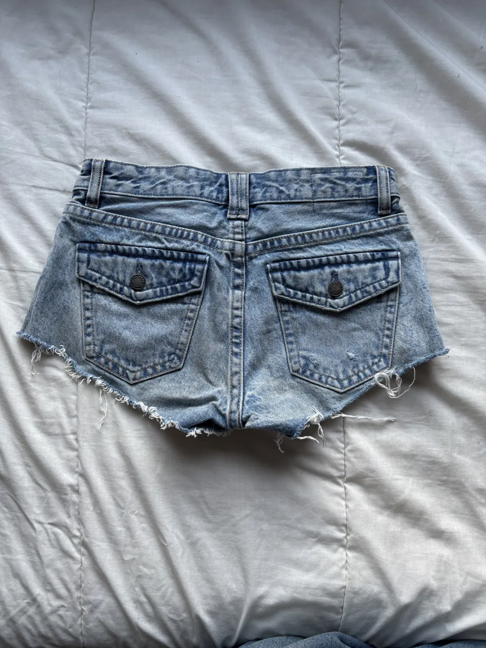 Shorts de jean con roturas y detalles deshilachados en los bordes. Posee bolsillos delanteros y traseros con tapa y botón.