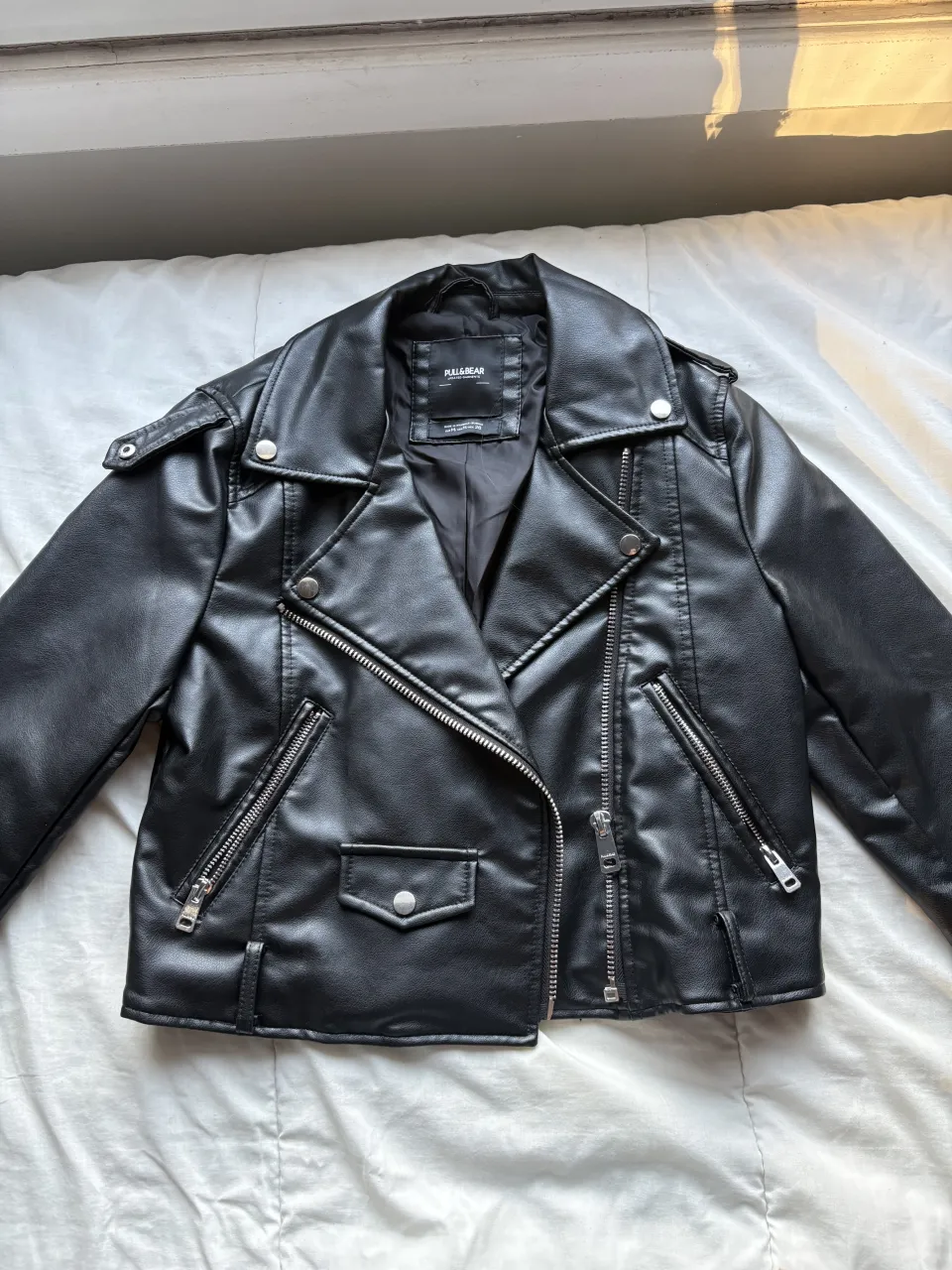Campera de cuero sintético negra, estilo biker, con cierre al frente, bolsillos con cierre y solapa, y cuello con solapas.