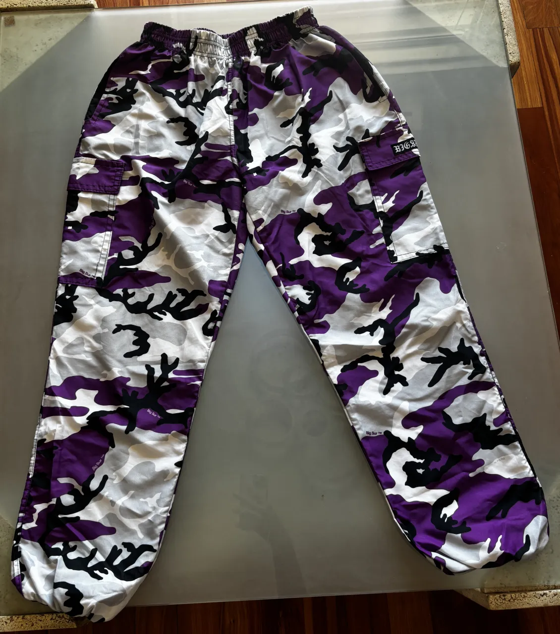 Pantalones cargo con estampado de camuflaje en tonos morado, blanco y negro. Cintura elástica y bolsillos.