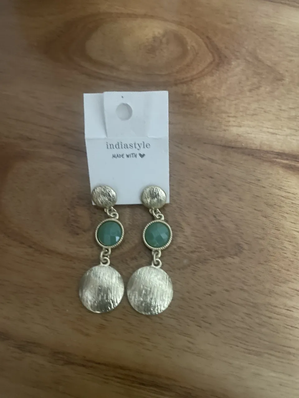 Aros colgantes dorados con piedra verde y detalle de disco texturizado. Un accesorio ideal para darle un toque chic a tu look.