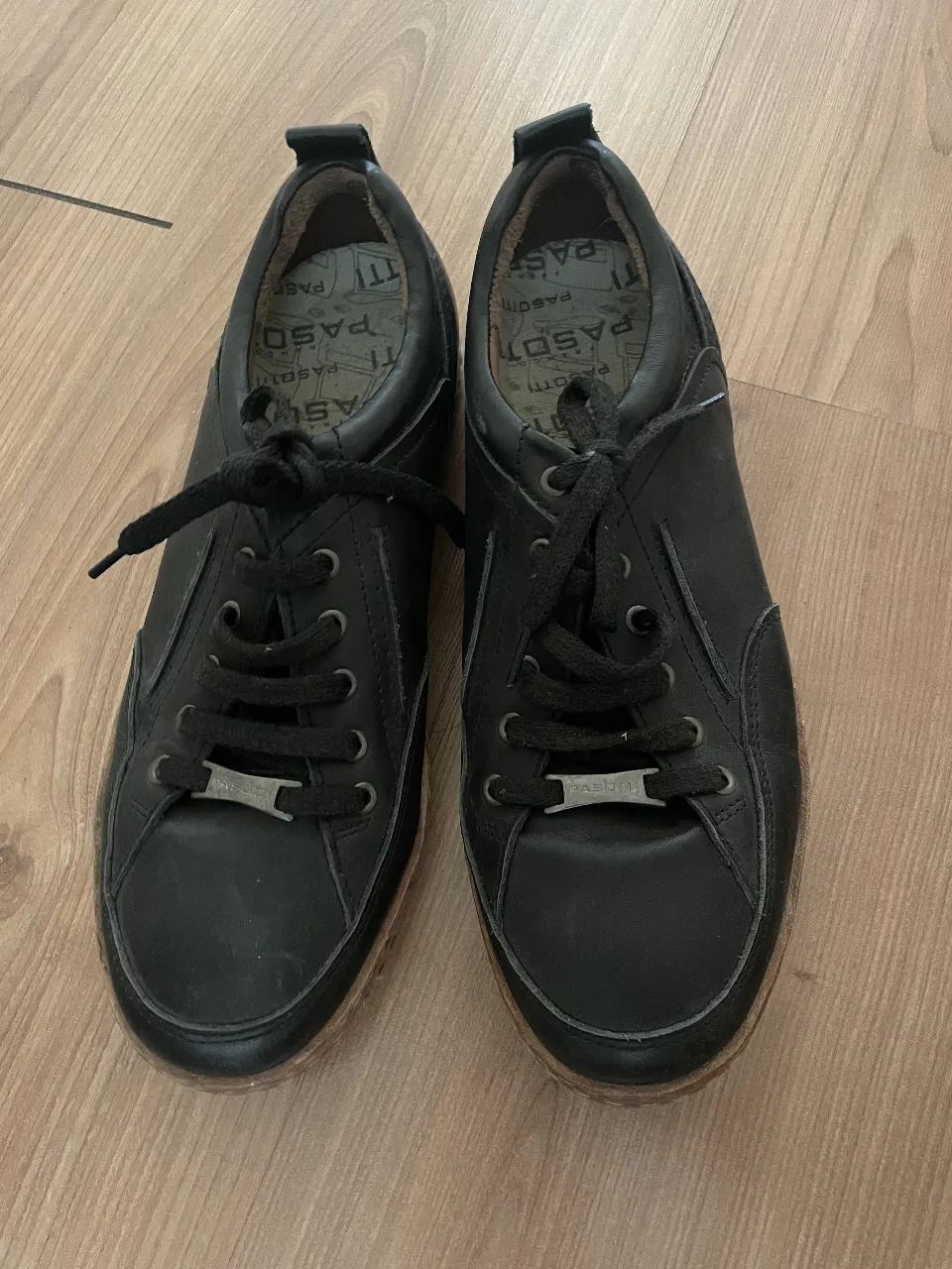 Zapatillas de cuero negras, estilo casual, con cordones y detalles de la marca Pasotti. Suela de goma.